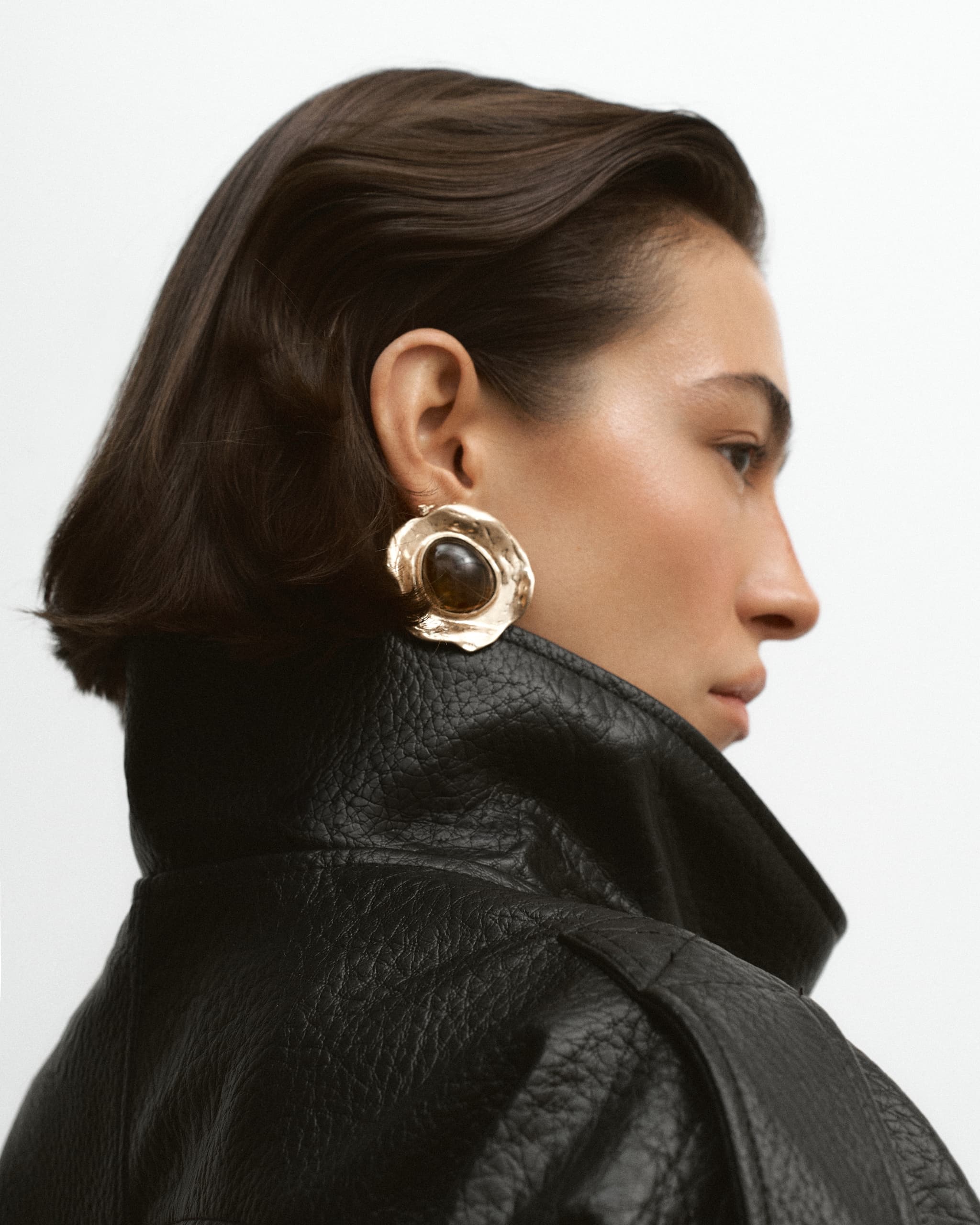 Profile view of a person in a leather jacket, wearing a large statement earring.