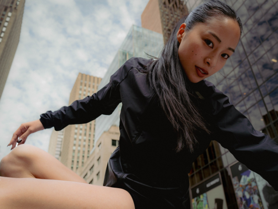 Person in black attire posing dynamically against a city skyscraper backdrop.