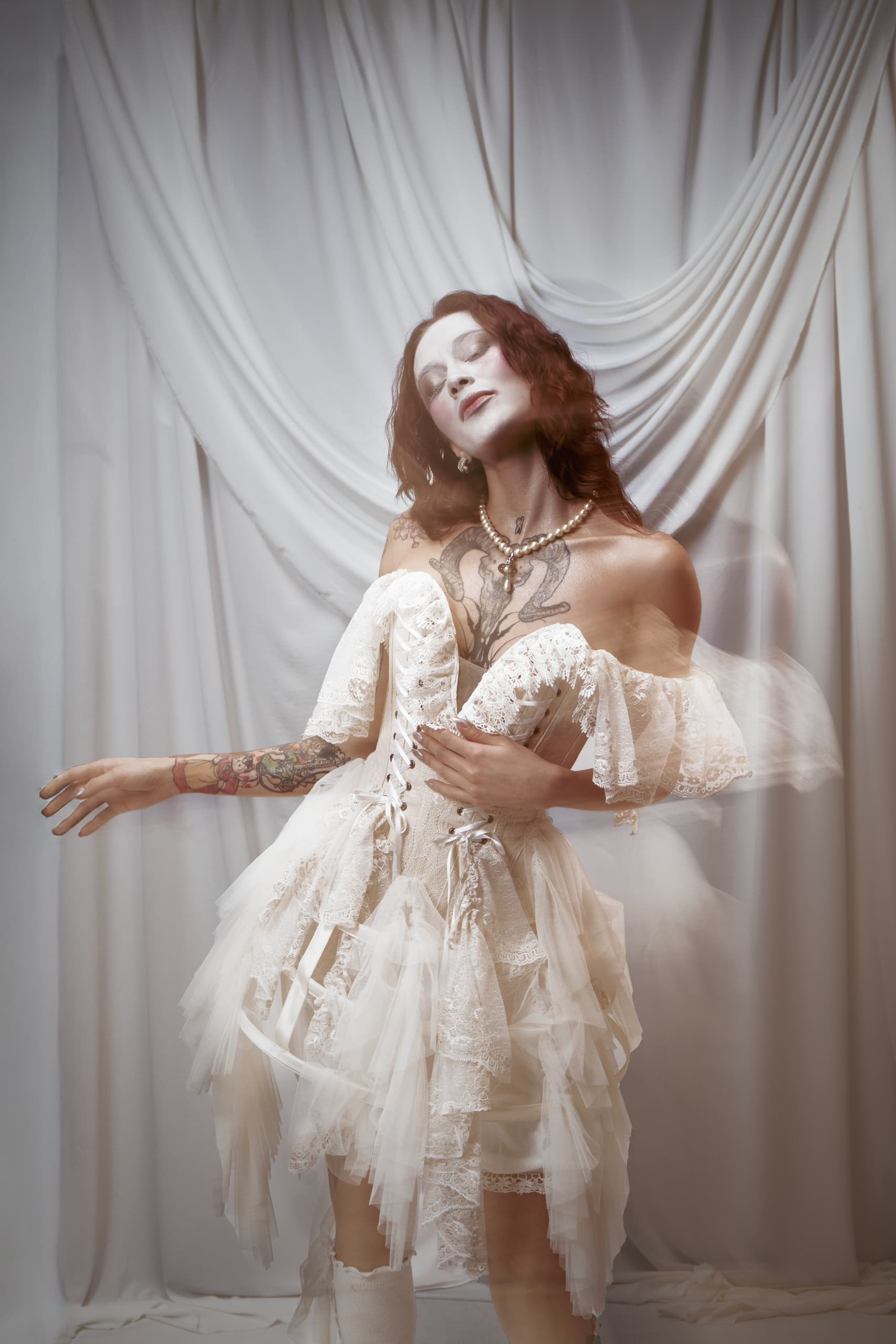 Person in flowing white dress with tattoos poses gracefully, modern gothic style.