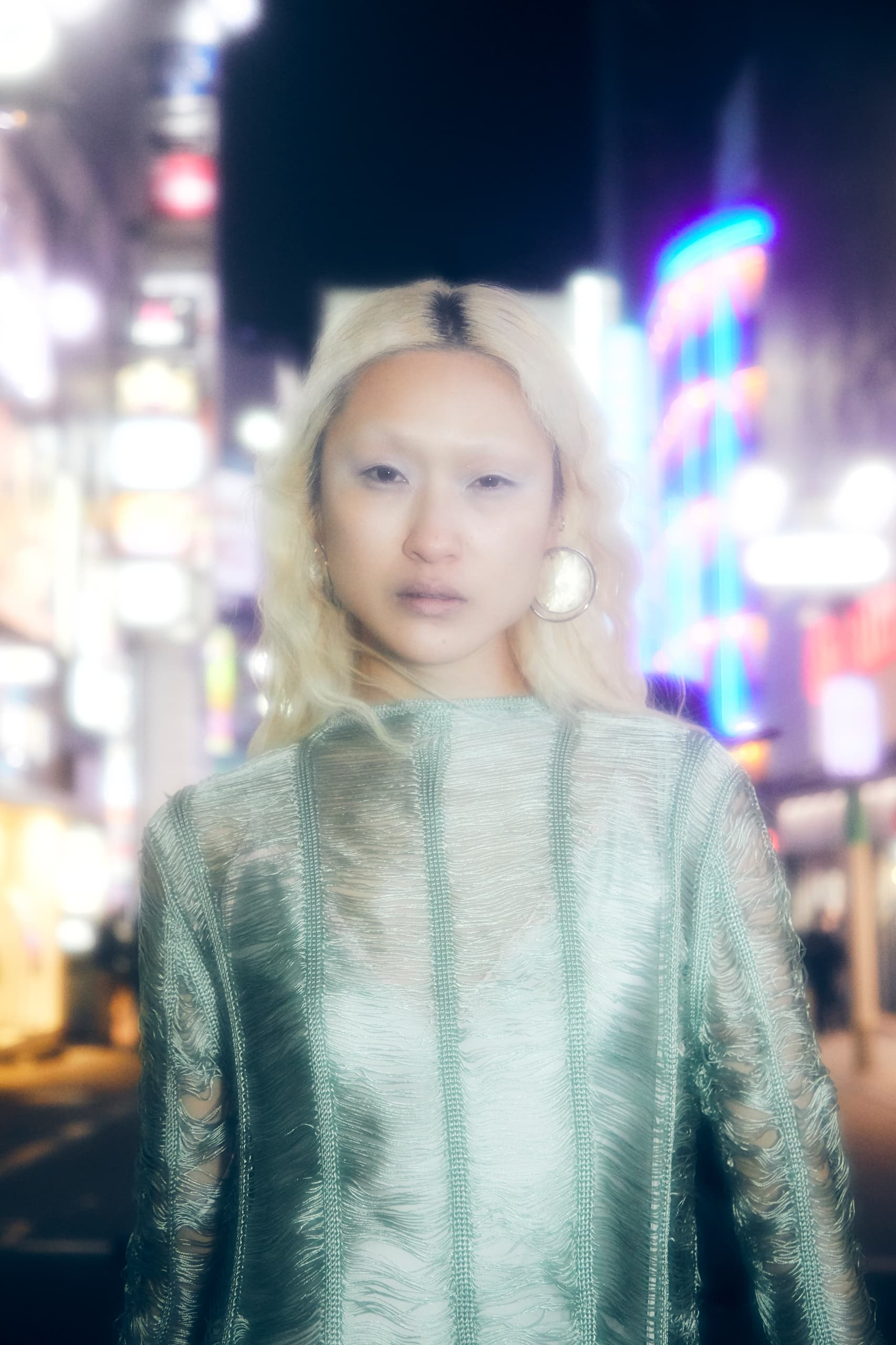 Person in green textured outfit with neon city lights at night. Fashion and nightlife vibes.