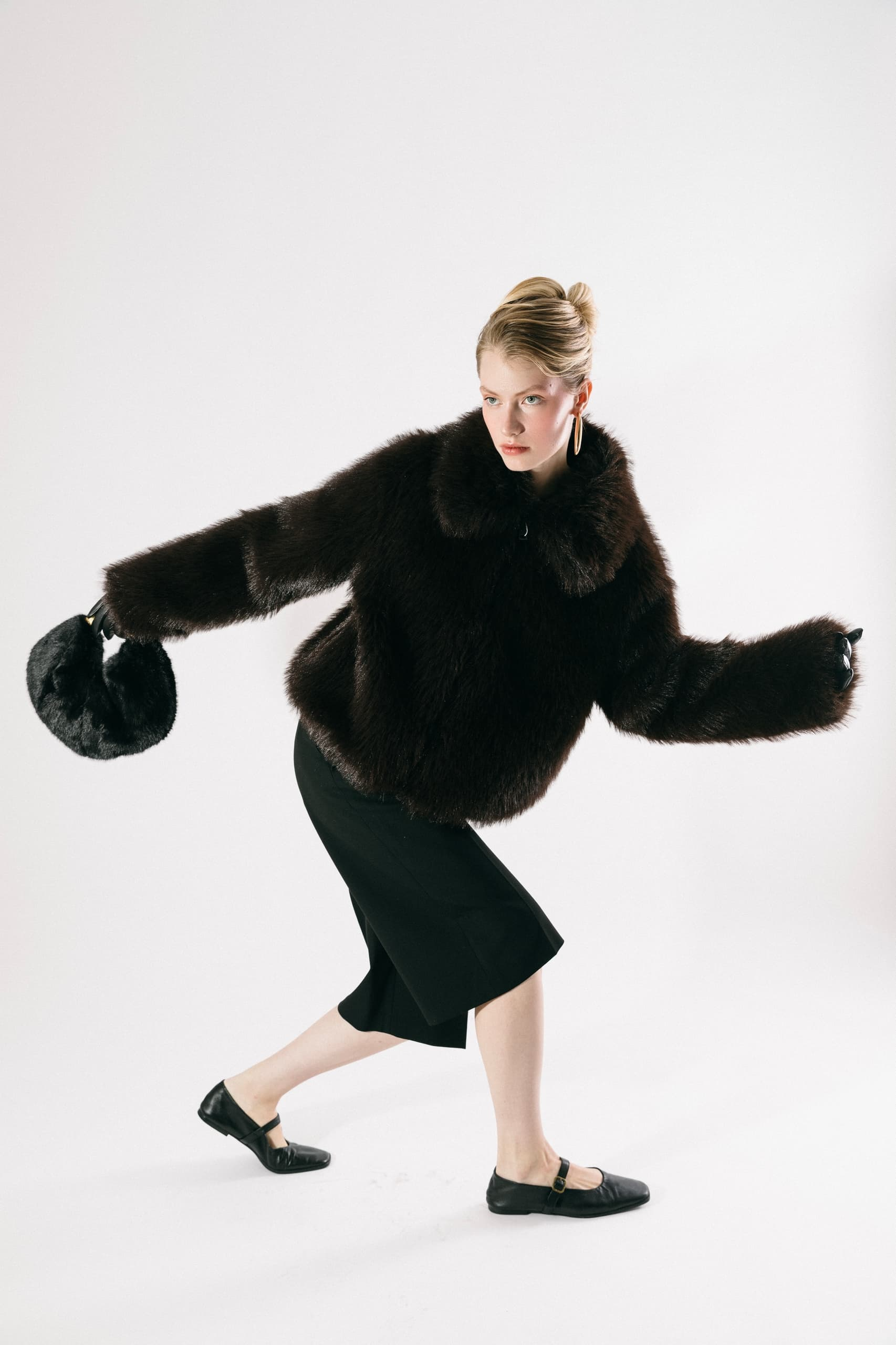 Fashion model in a fur jacket and skirt posing stylishly against a plain background.