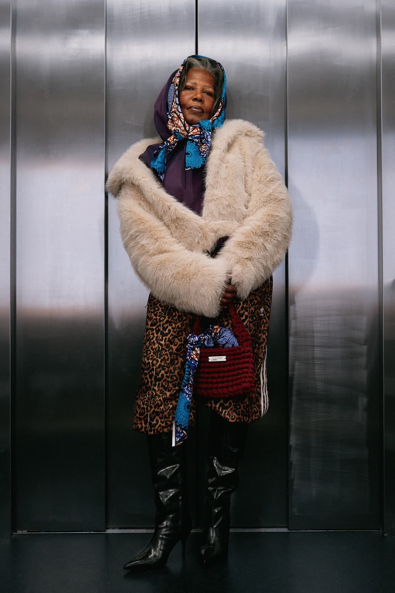 Stylish woman in fur coat and boots, with patterned scarf in a modern setting.