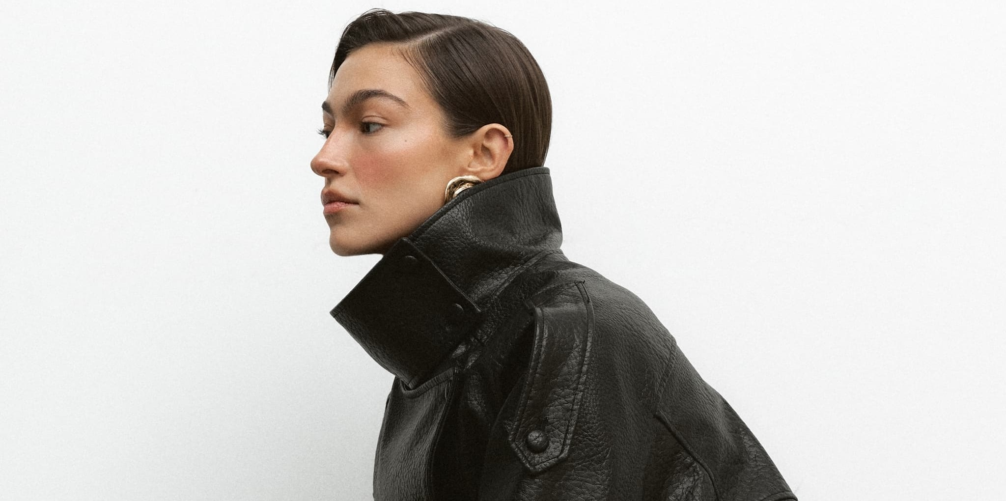 Portrait of a woman in a stylish black leather jacket and bold gold earrings.