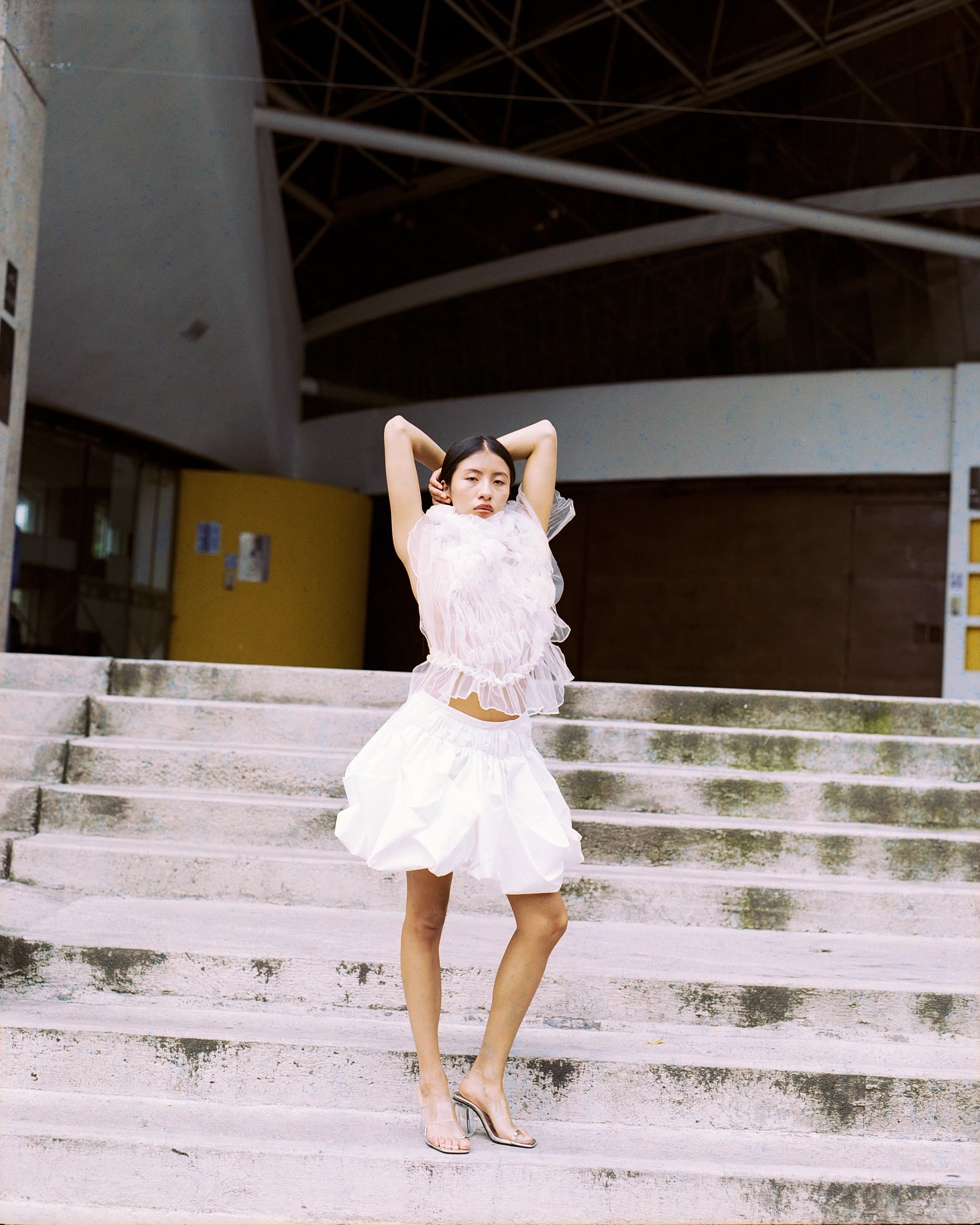 Fashionable woman in white dress on steps, striking a confident pose.