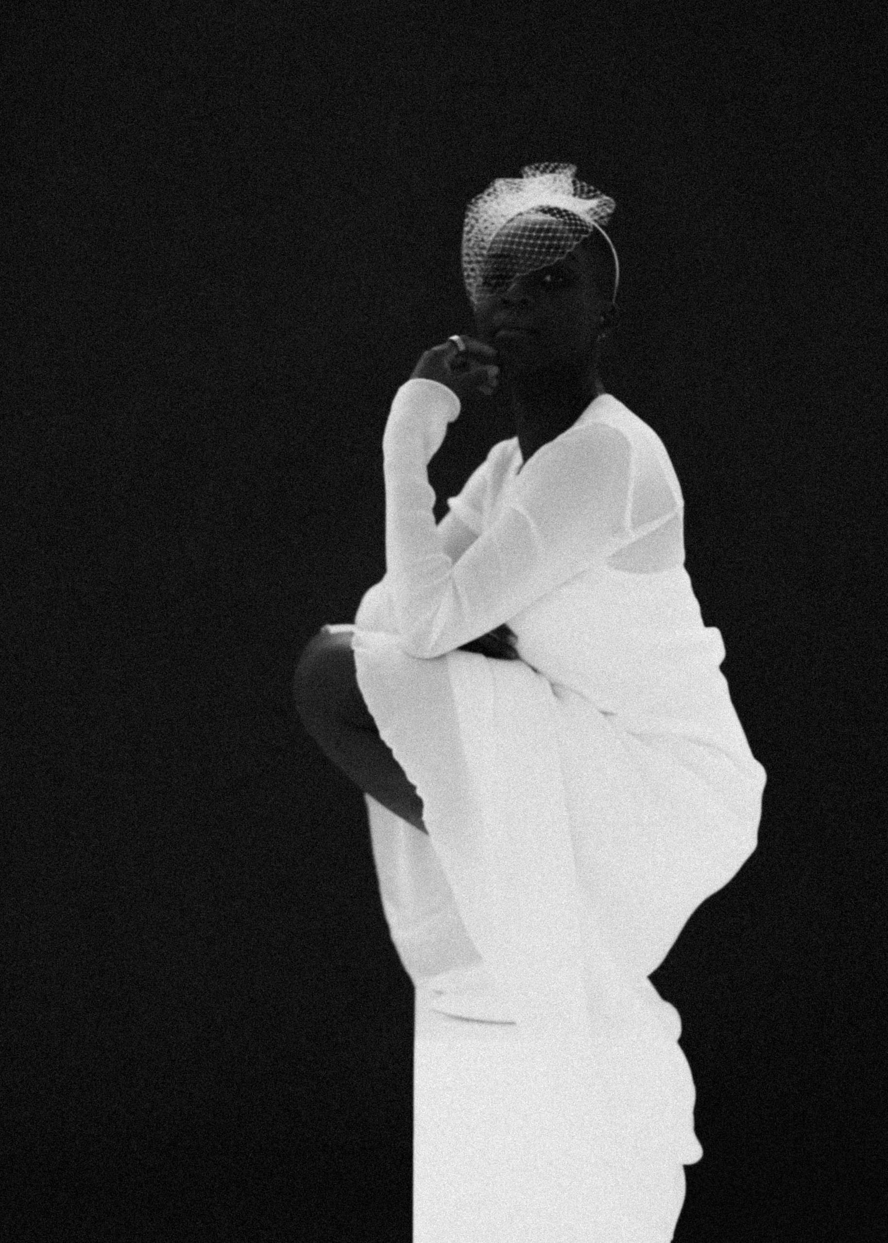 Elegant person in white dress and veil posing against black background.