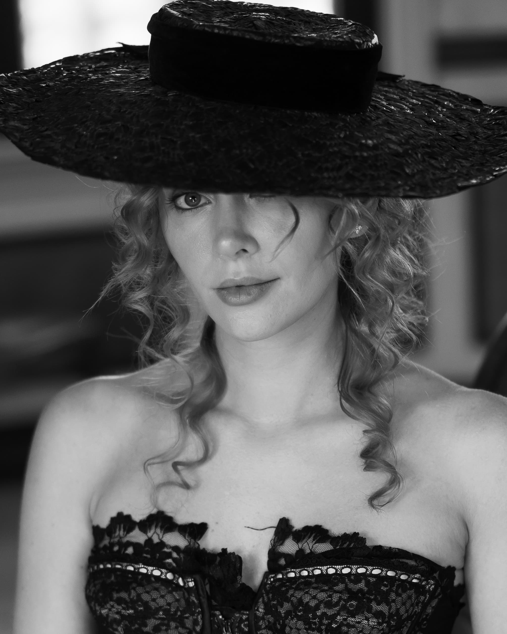 Woman in lace dress wearing wide-brimmed hat, black and white portrait.