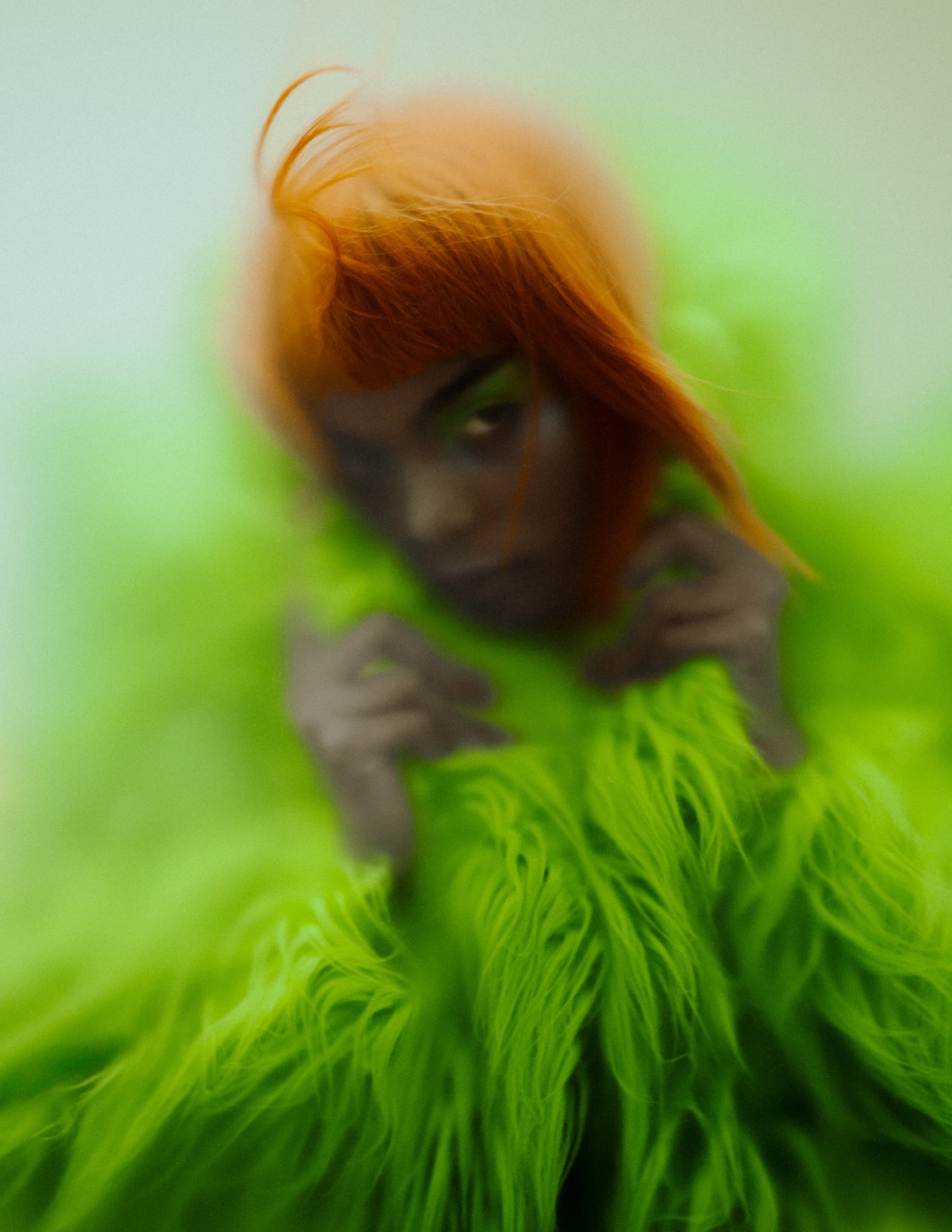 Vibrant orange hair complements bold green fur fashion, artistic and avant-garde style.