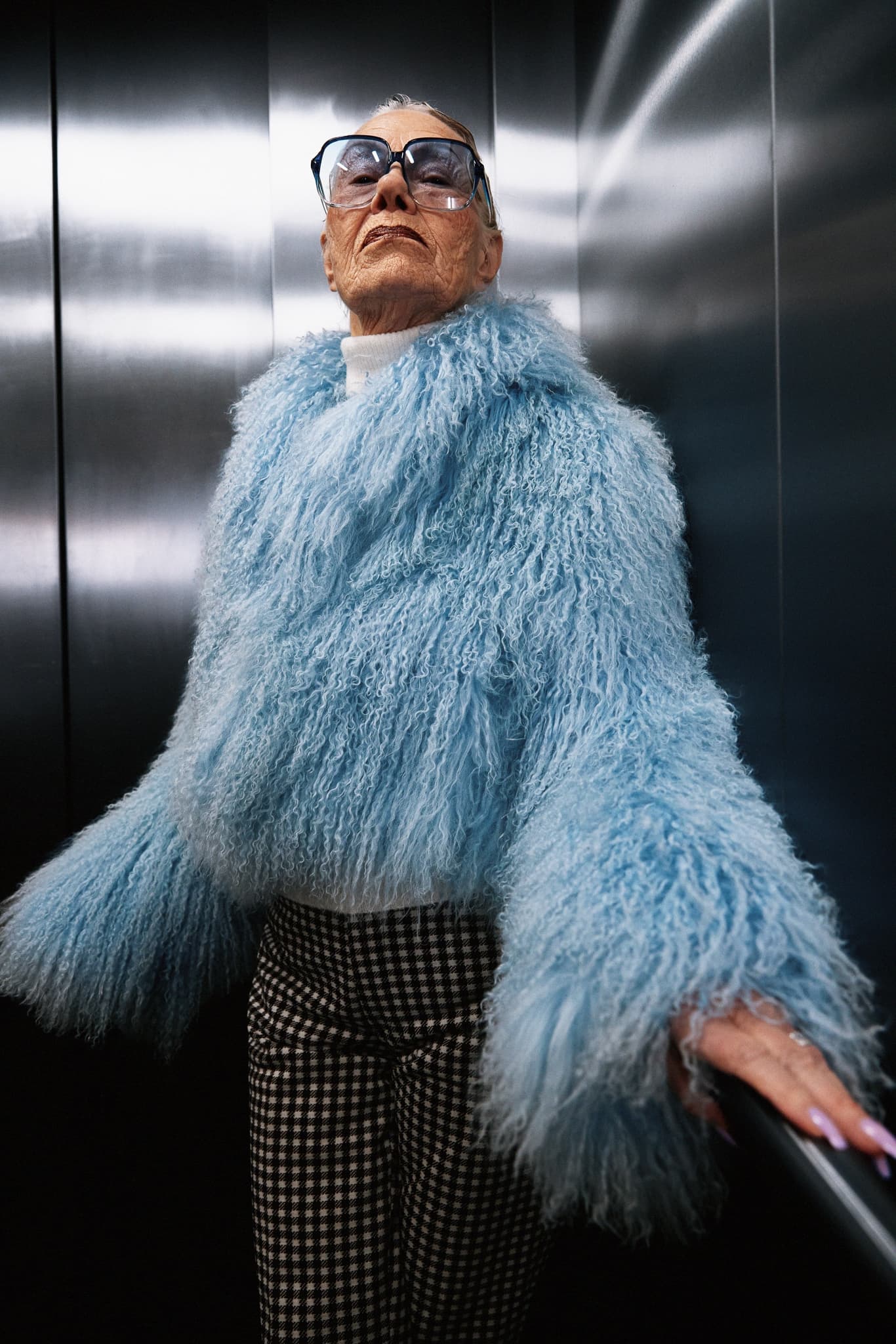 Stylish senior in blue fur coat and glasses in elevator.