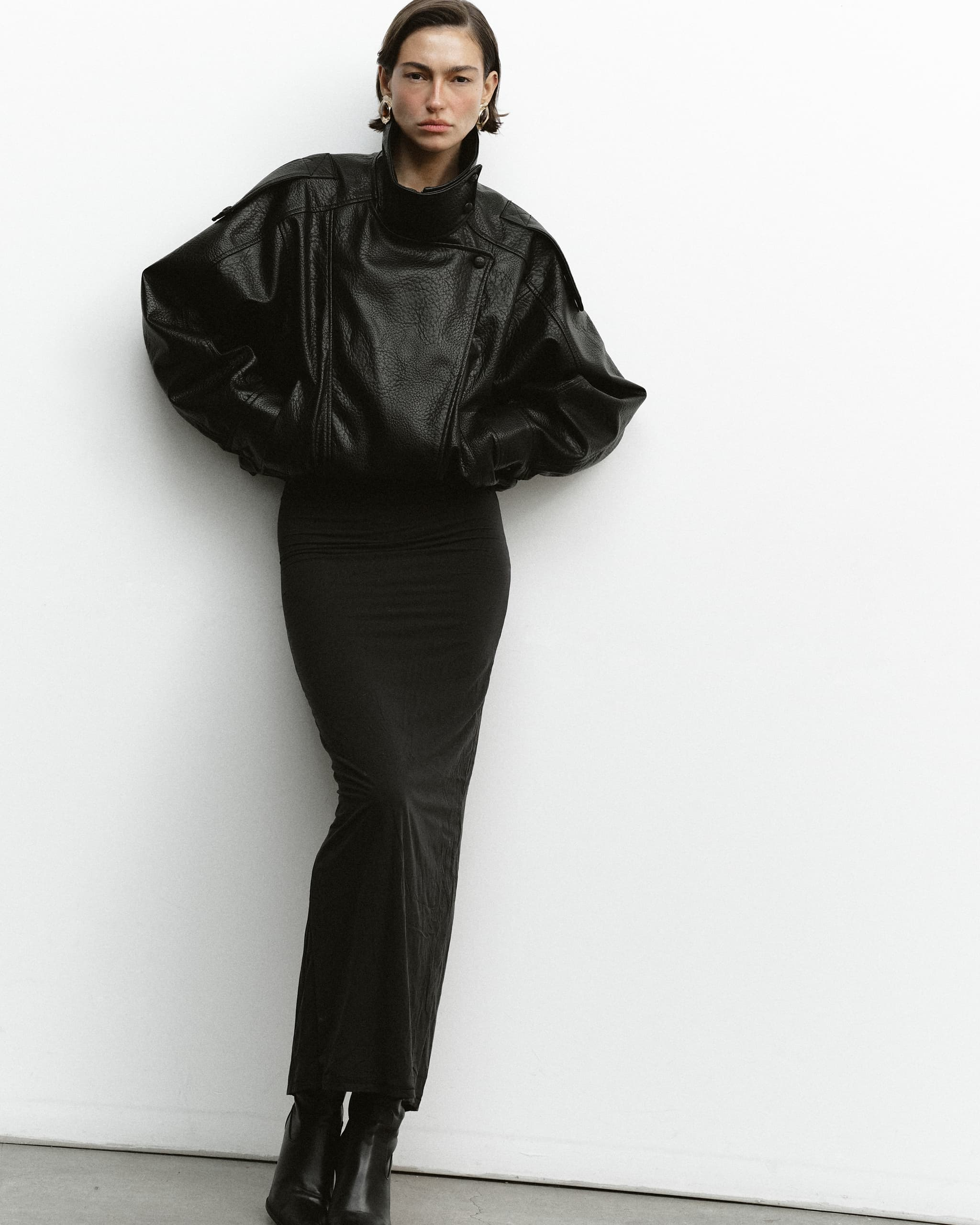 Fashionable woman in black leather jacket and dress, against a white background.