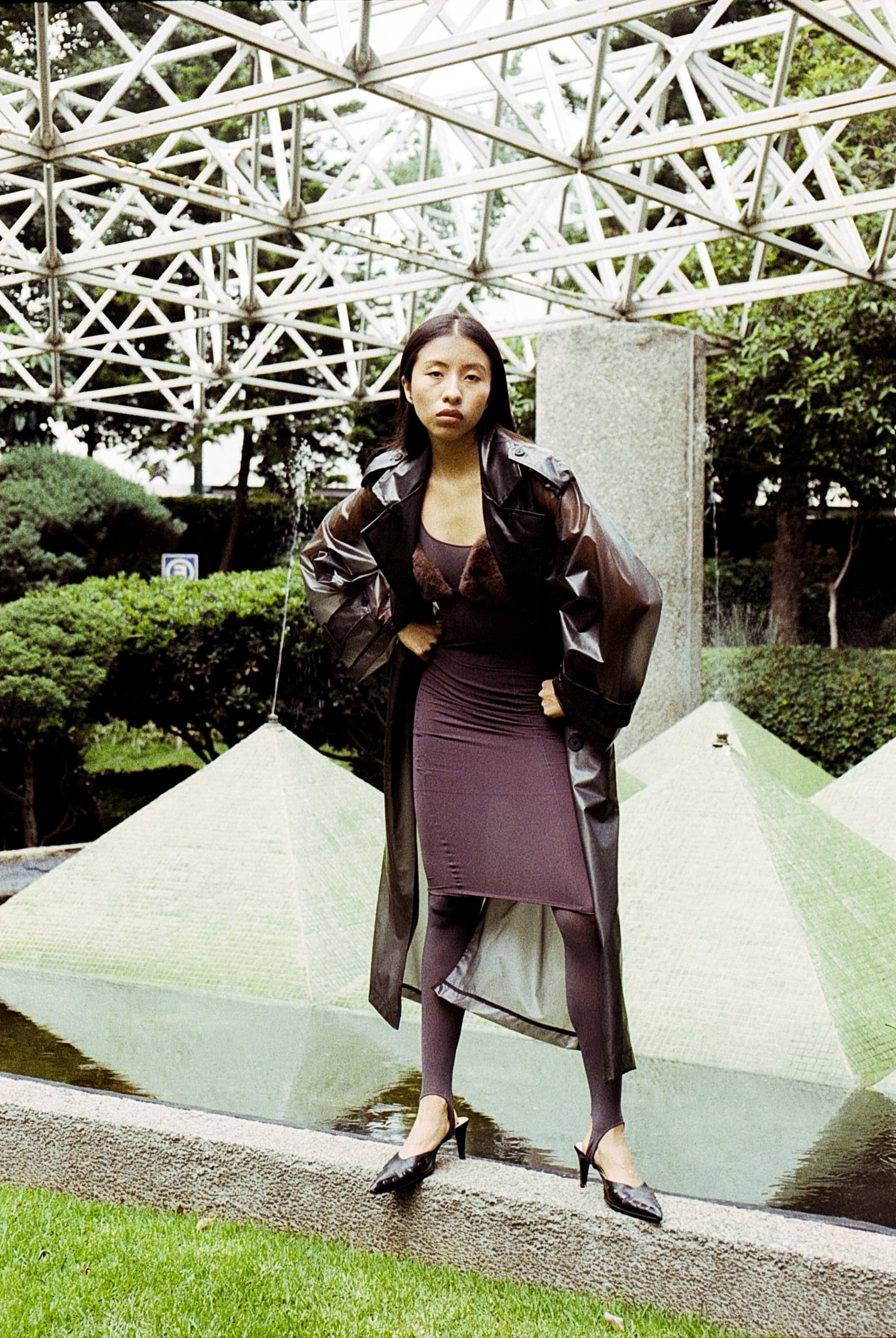 Stylish woman in a futuristic coat posing by outdoor geometric sculptures.