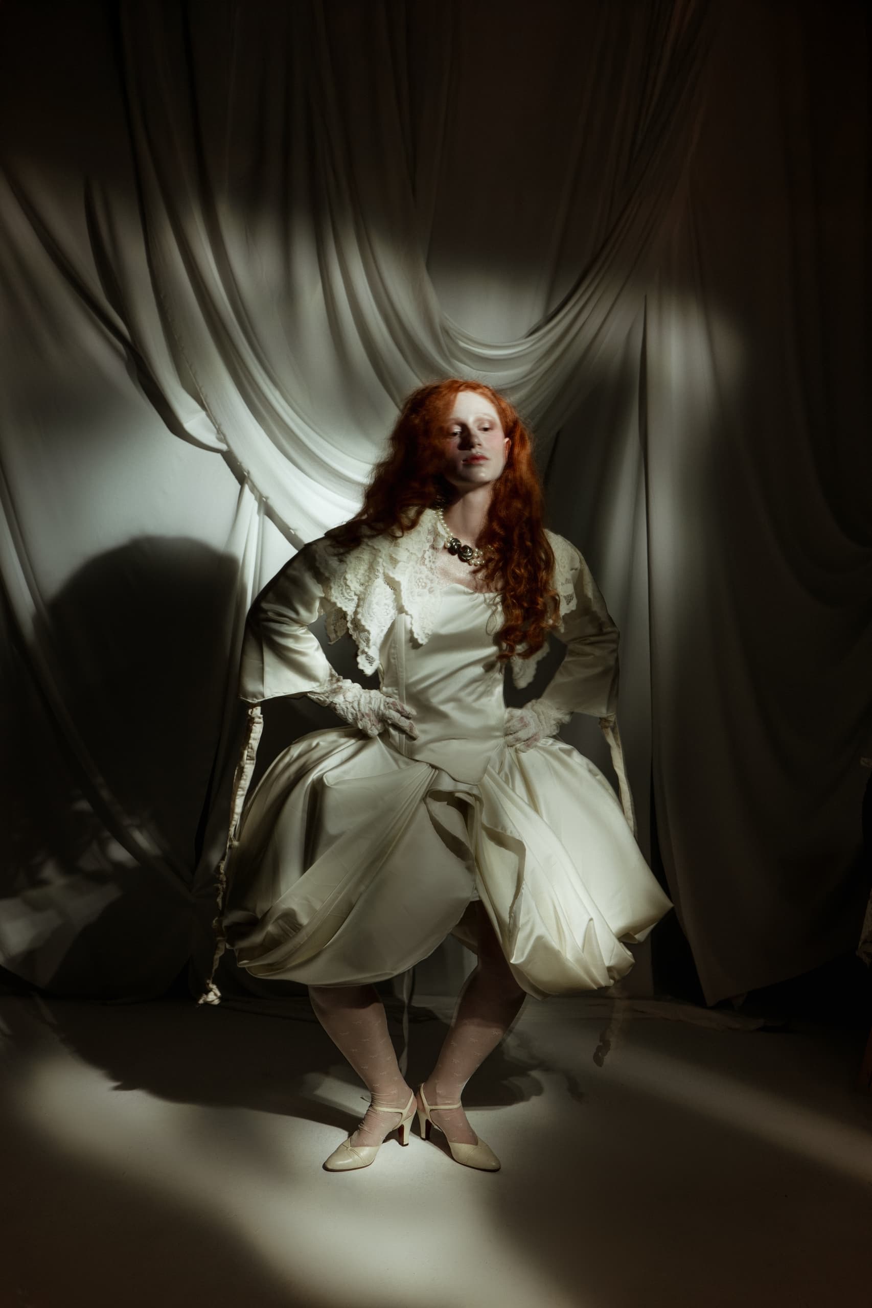 Elegant woman in vintage white gown against dramatic draped fabric backdrop.