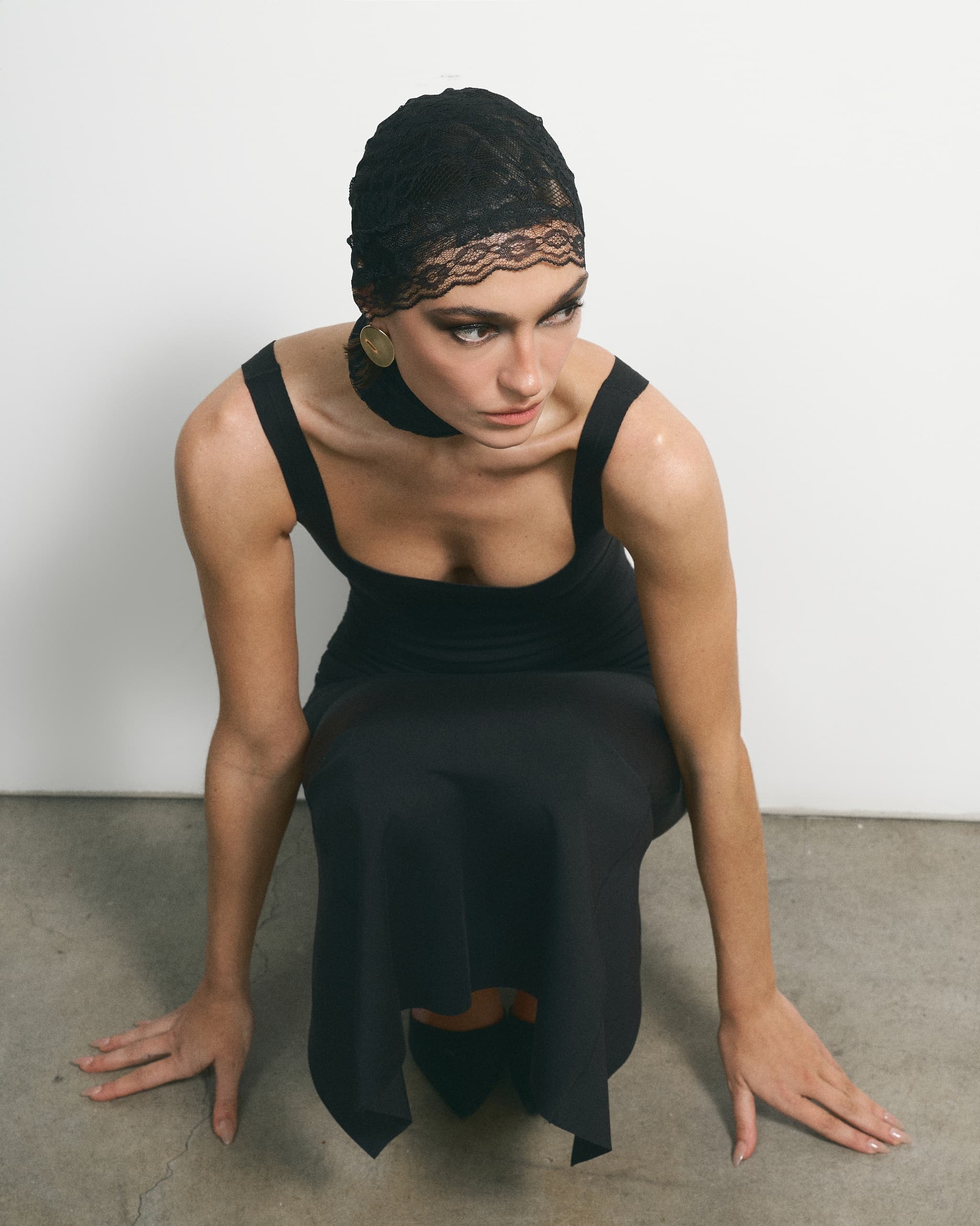Woman in black dress and lace headscarf sitting on floor, posing elegantly.