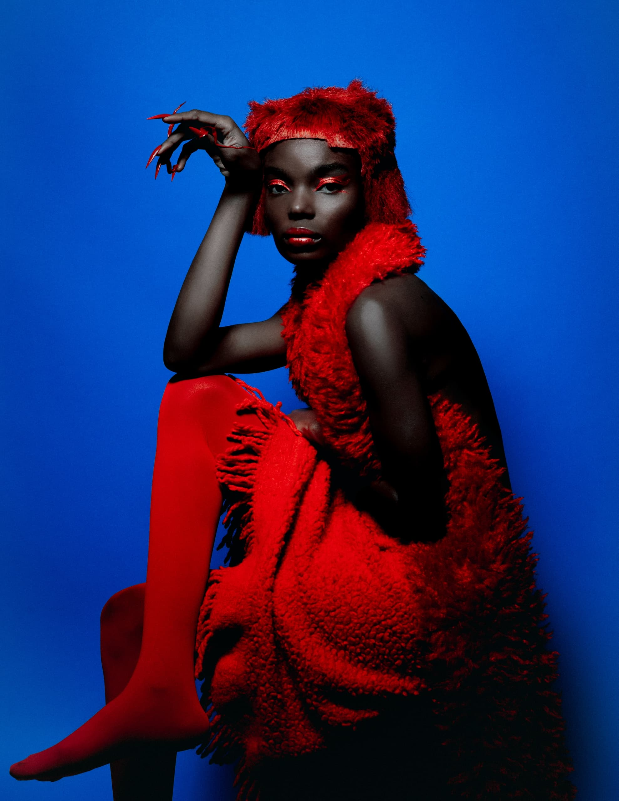 Bold fashion in red fur and vibrant makeup, striking pose on a vivid blue background.