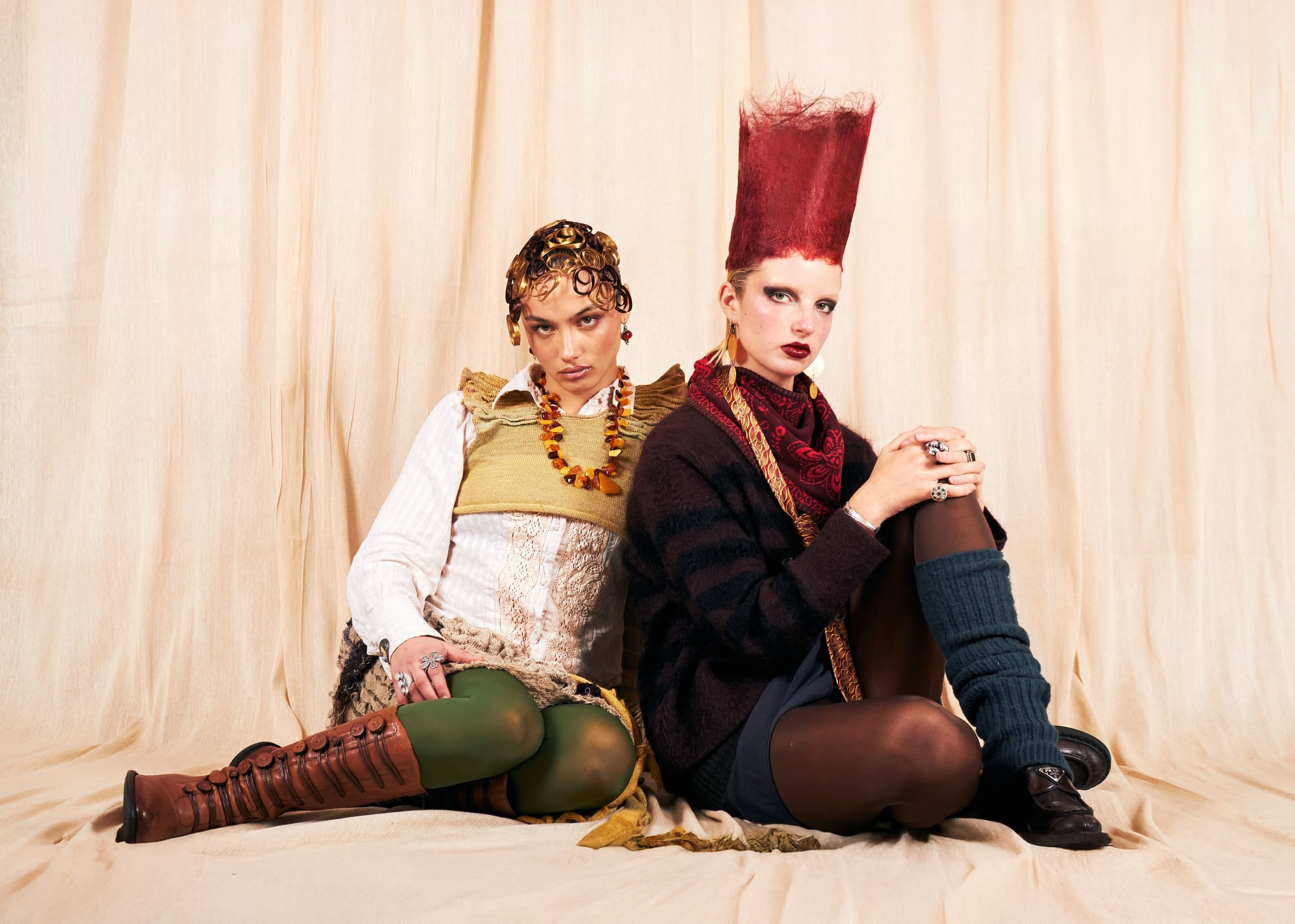 Fashionable duo showcasing eclectic style in chic, avant-garde outfits against fabric backdrop.