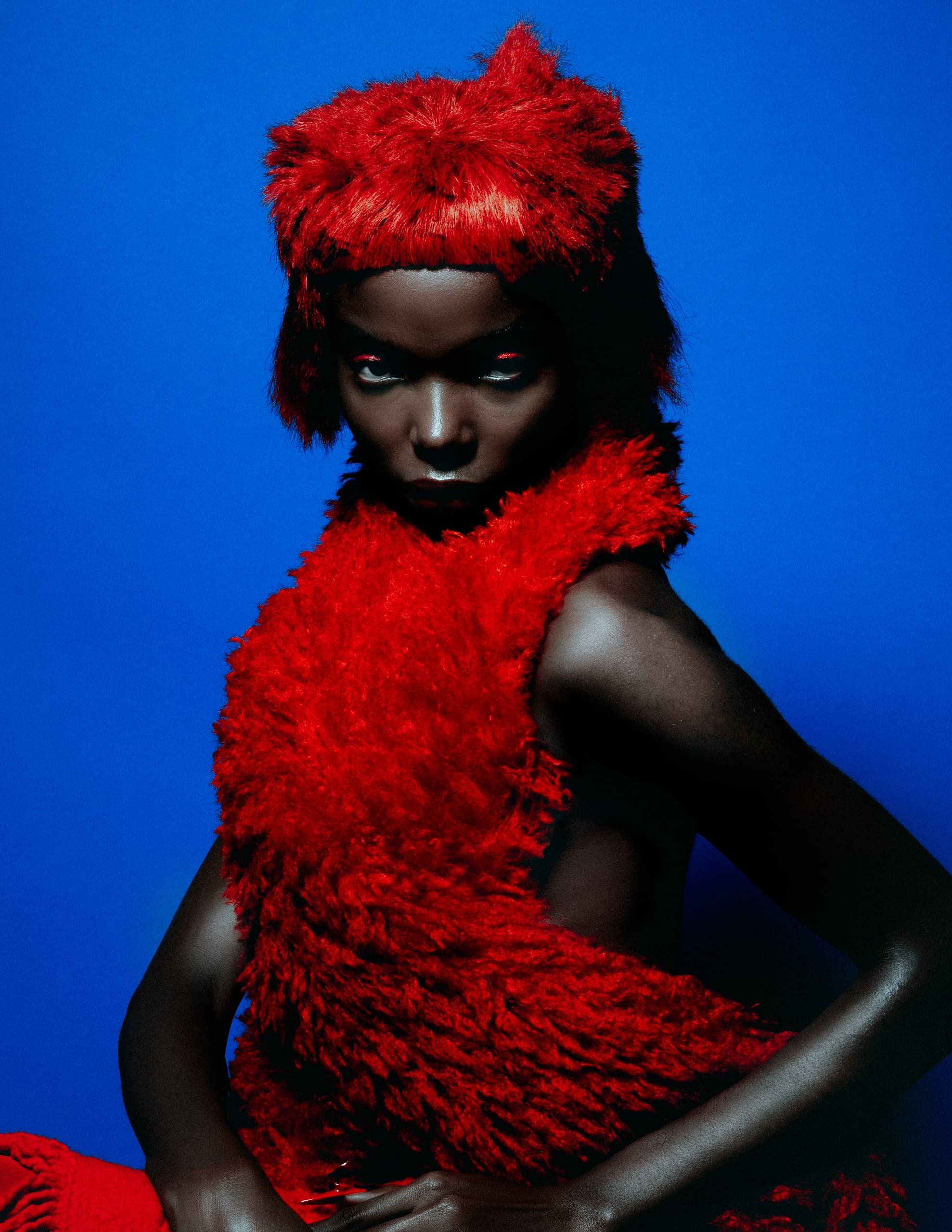 Model in vibrant red fur outfit against a striking blue background.