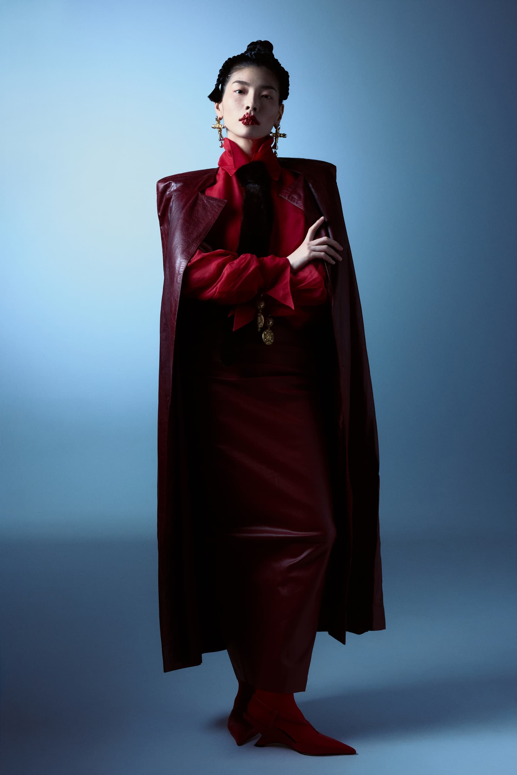 Fashion model in red leather ensemble with bold lipstick and statement earrings.