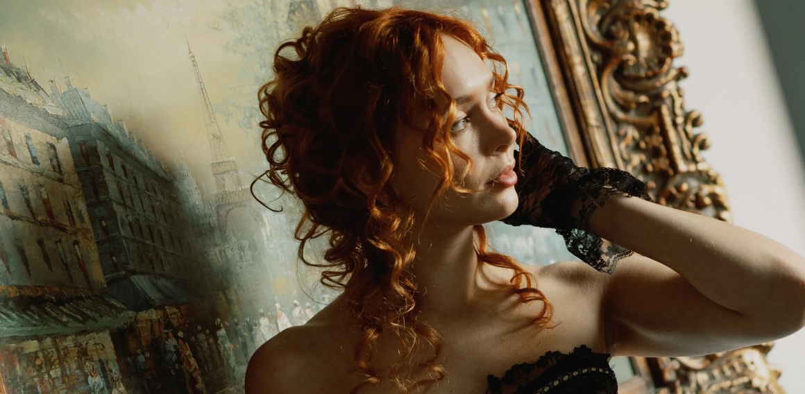 Woman poses elegantly by a vintage painting with ornate frame.