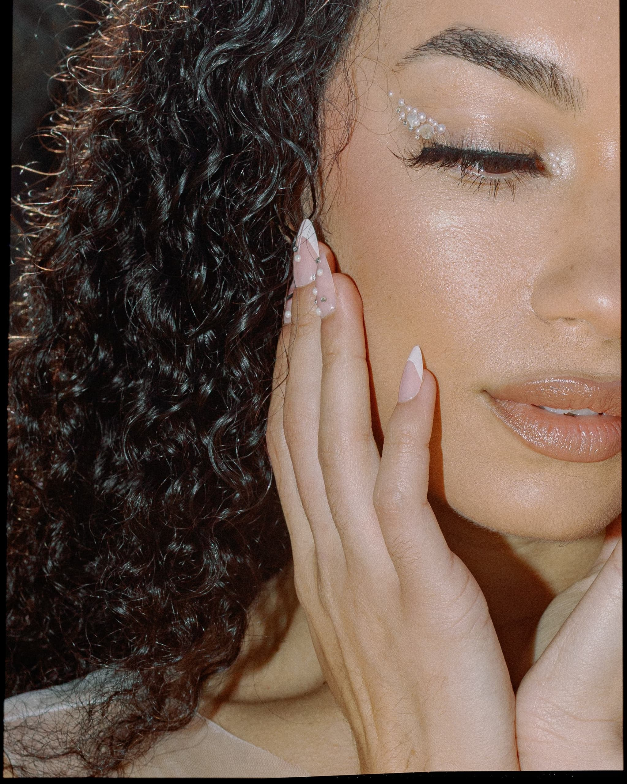 Close-up of a woman with pearl eye makeup and elegant hand pose.