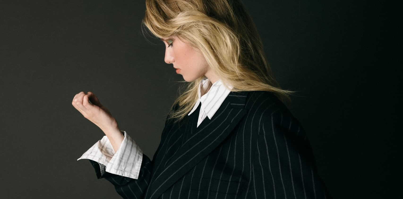 Woman in pinstripe suit with side-swept hair, profile view.