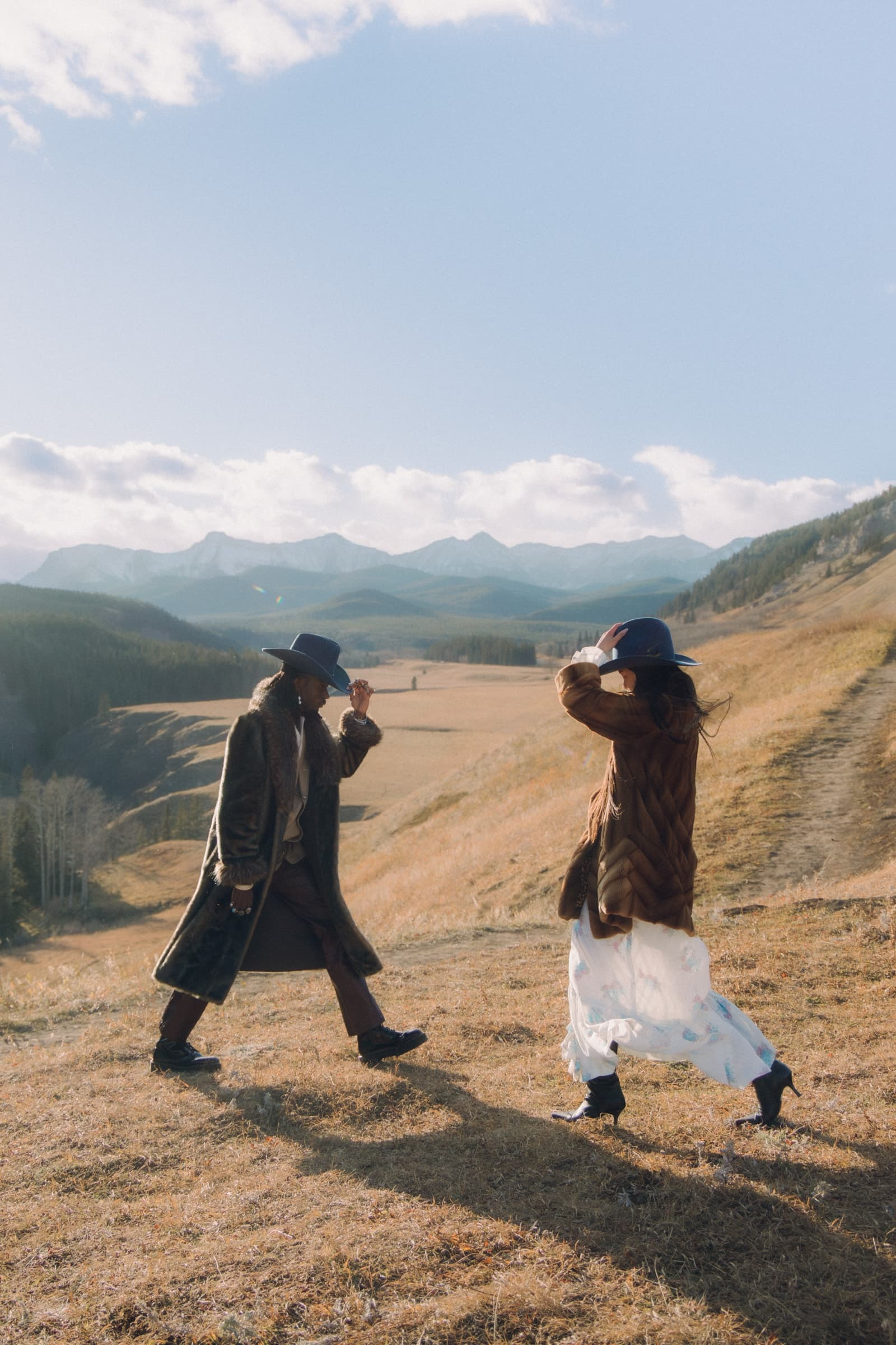 Two people in hats enjoy walking on a scenic mountain trail.