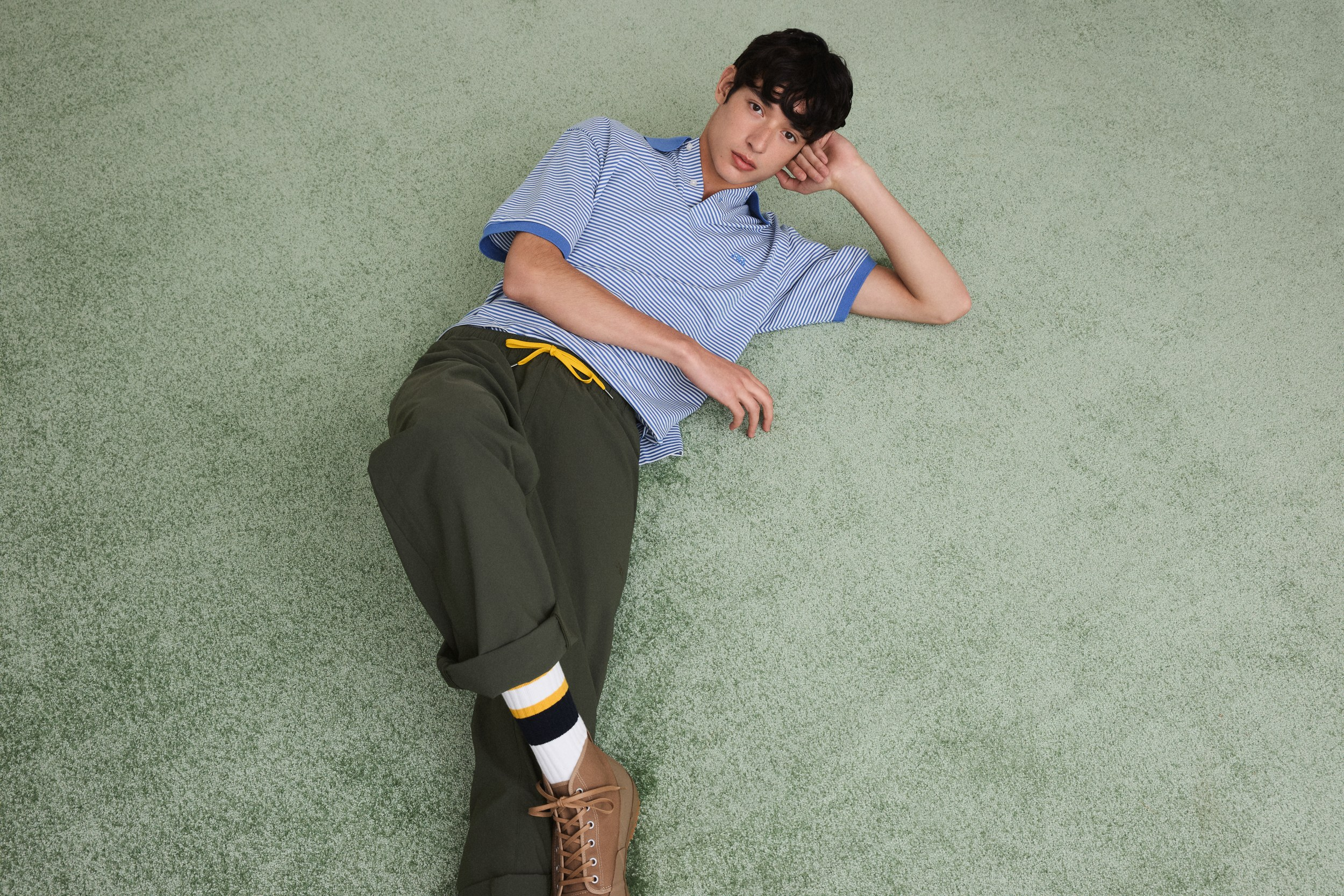 Man in casual outfit lying on green carpet, striped shirt, relaxed pose.