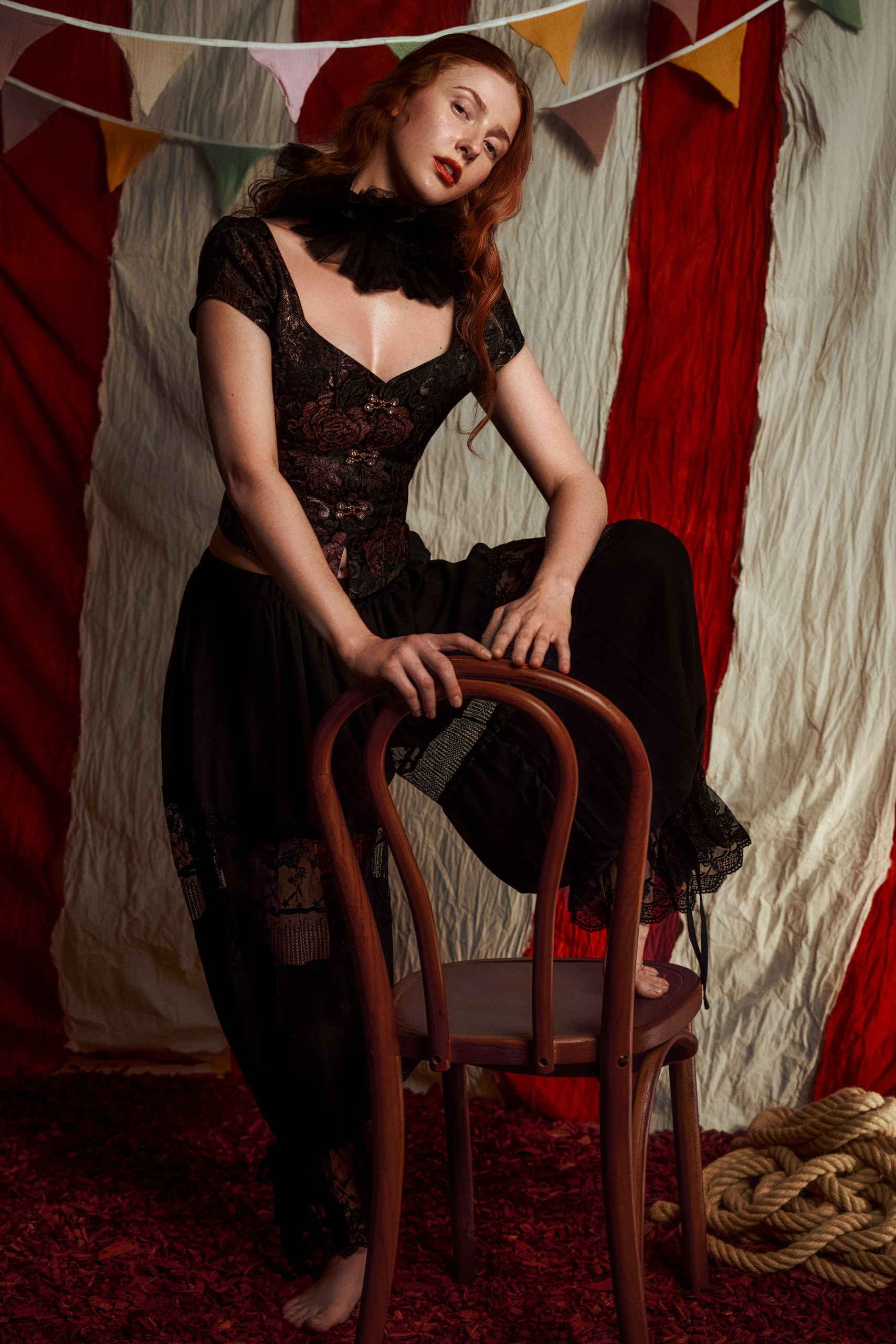 Vintage circus fashion with model on chair in colorful tent setting.