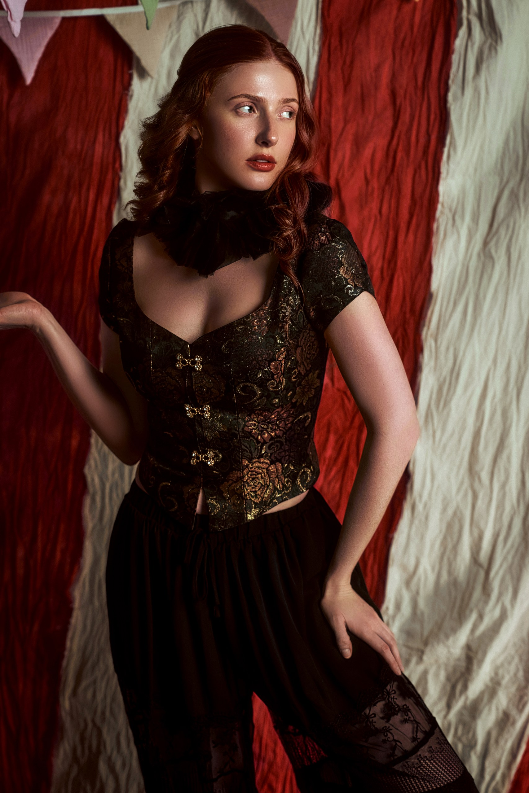 Woman in vintage attire posing against red and white fabric backdrop.