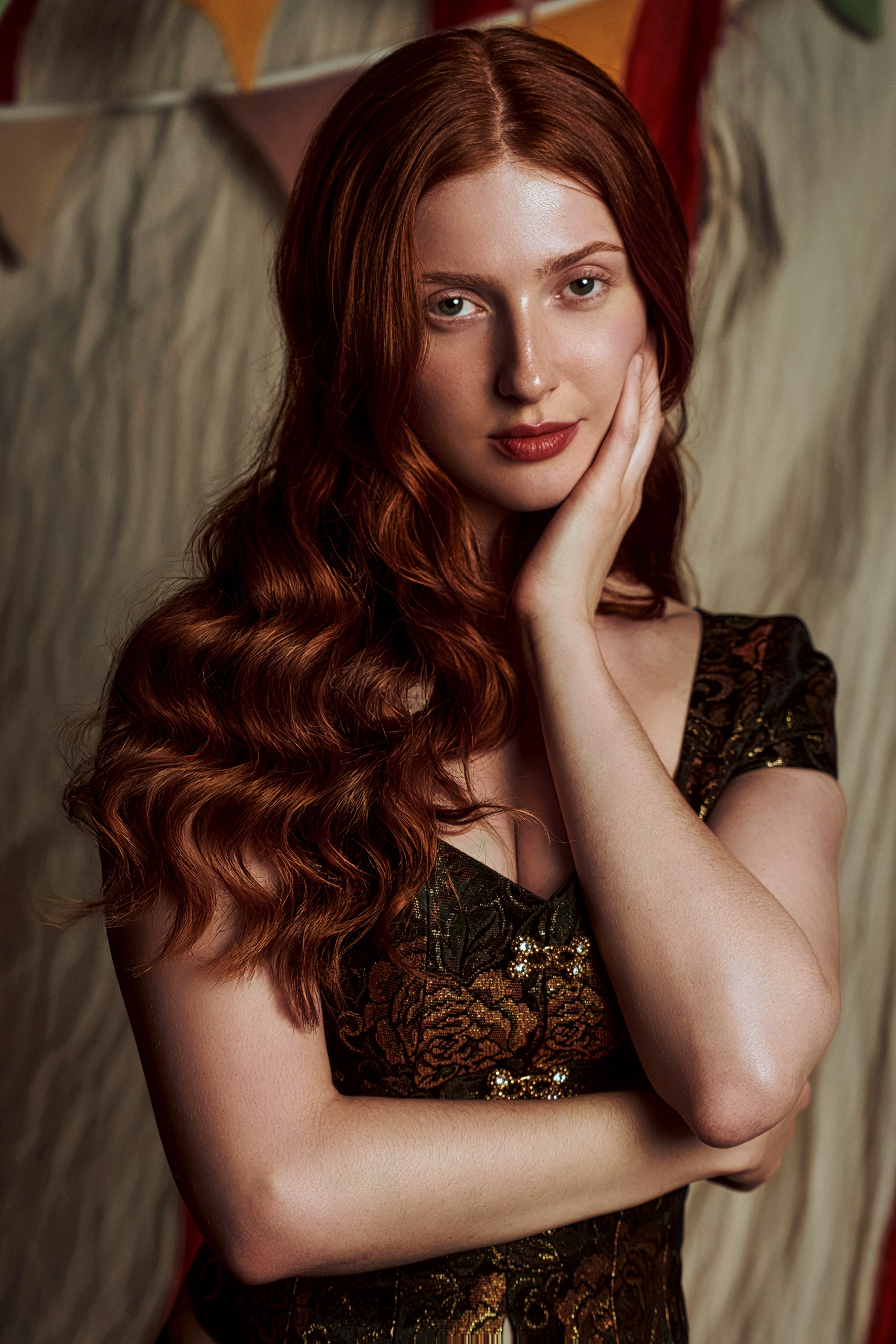 Woman with long red hair in elegant dress, posing gracefully indoors.