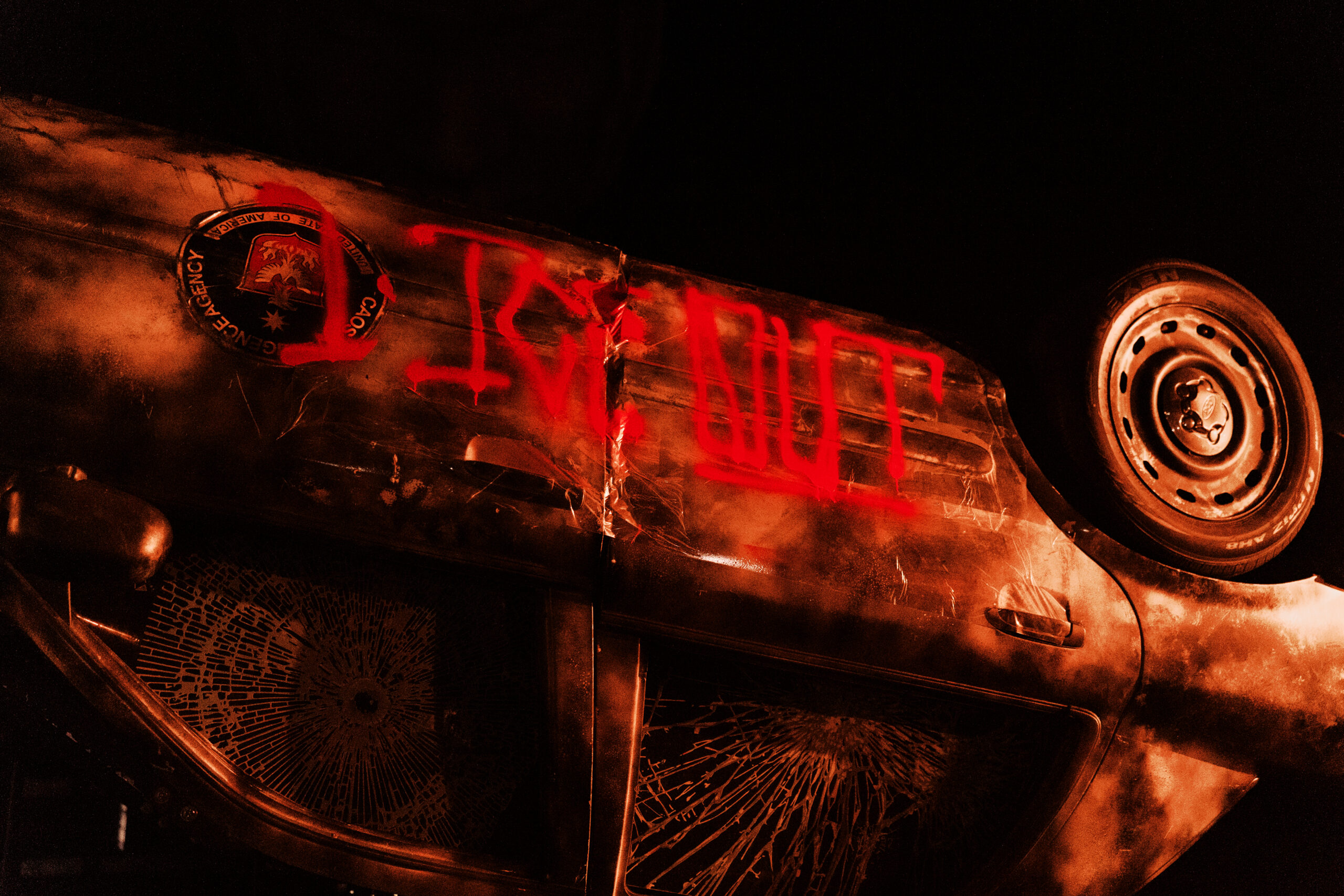 Overturned car with red graffiti and shattered windows at night.