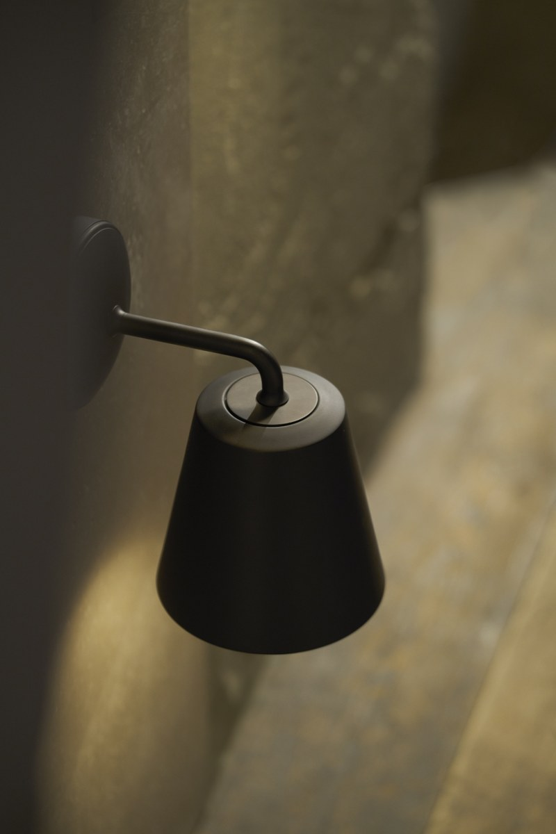 Black wall-mounted metal lamp with soft lighting on textured surface.