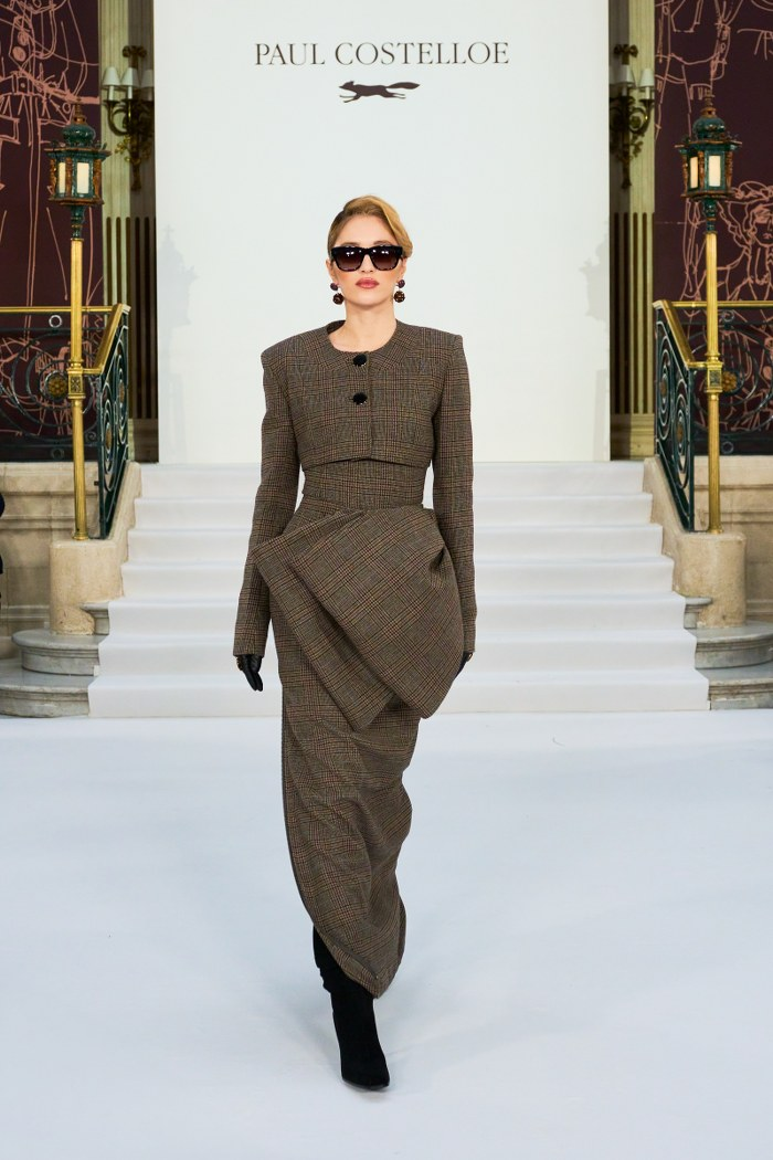Fashion model in elegant brown plaid outfit on runway stairs.