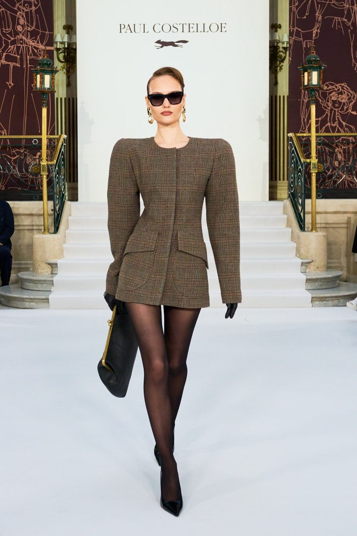 Model in a chic dress and sunglasses walking on runway stairs.