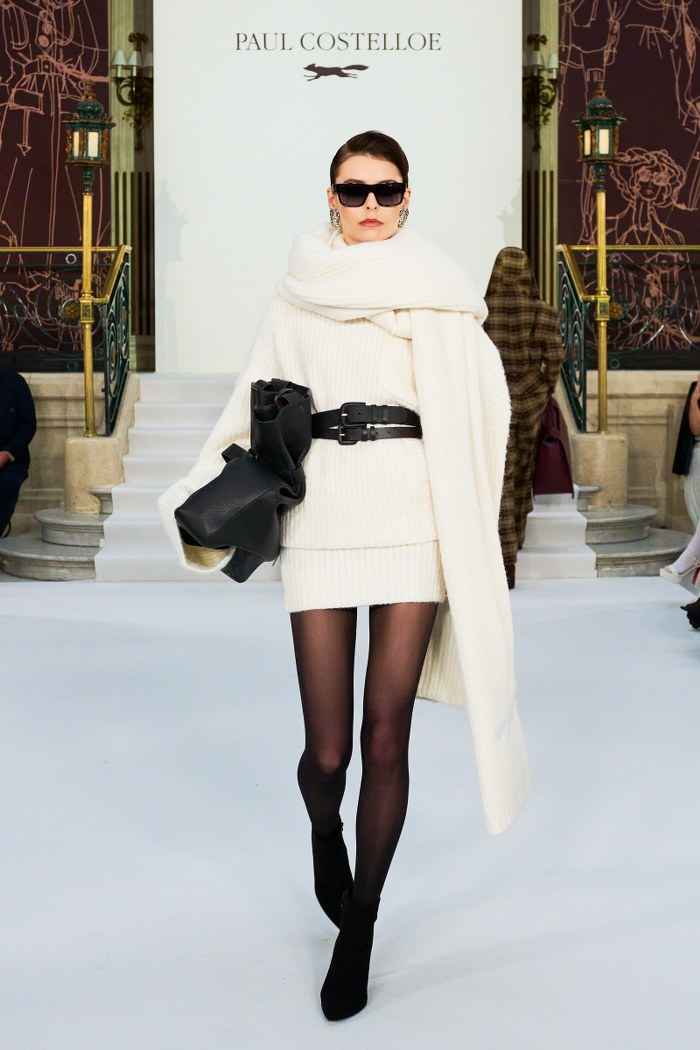 Model in chic winter fashion outfit walks runway in elegant setting.