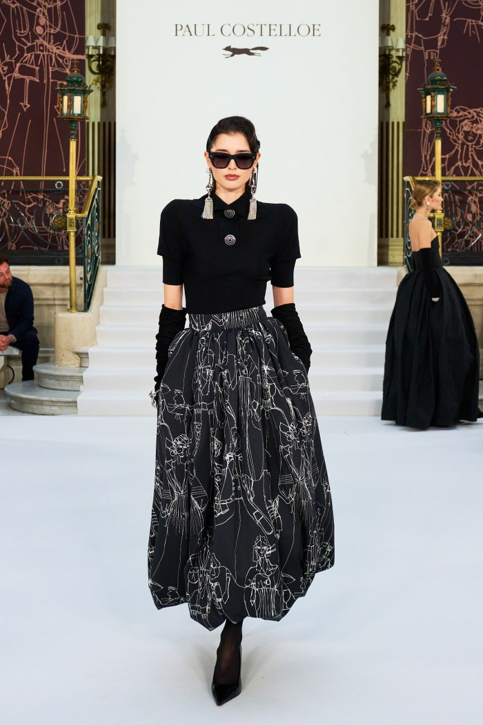 Model wearing black designer dress on runway at Paul Costelloe fashion show.