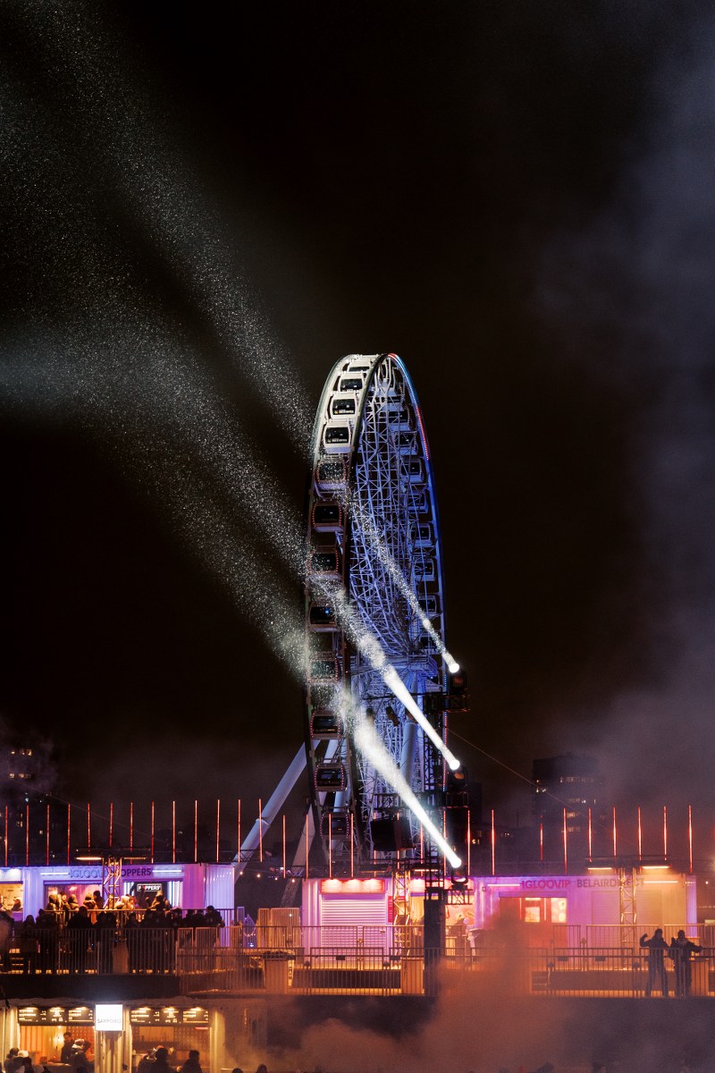 Nighttime Ferris wheel with colorful lights and fog at an amusement park.