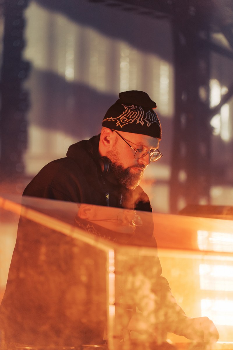 DJ performing in warm lighting, wearing a beanie and headphones indoors.