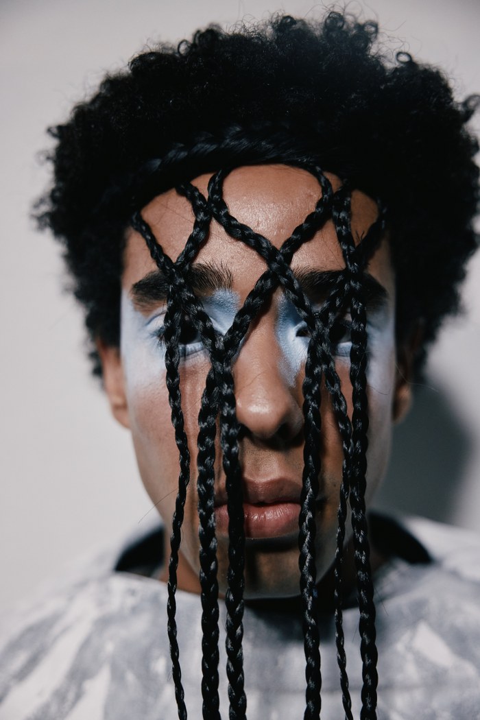 Artistic portrait with braided hair covering face, blue makeup accents eyes.