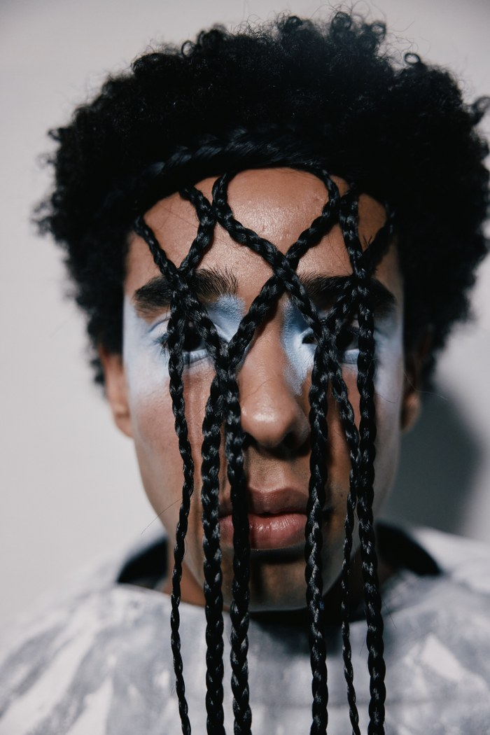 Artistic portrait with braided hair covering face, blue makeup accents eyes.