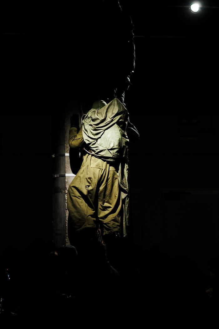 Dimly lit figure climbing a pole in a dark setting.