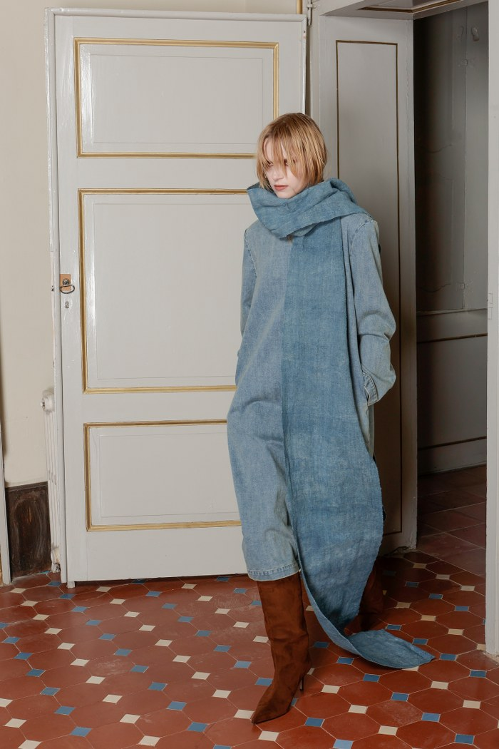 Woman in stylish blue oversized outfit and brown boots in elegant room.