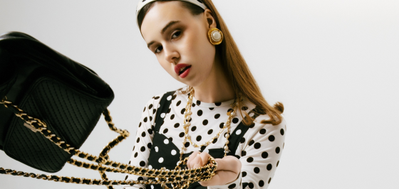 Fashionable woman holds stylish black bag with gold chain in polka dot outfit.