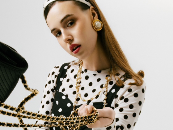 Fashionable woman holds stylish black bag with gold chain in polka dot outfit.