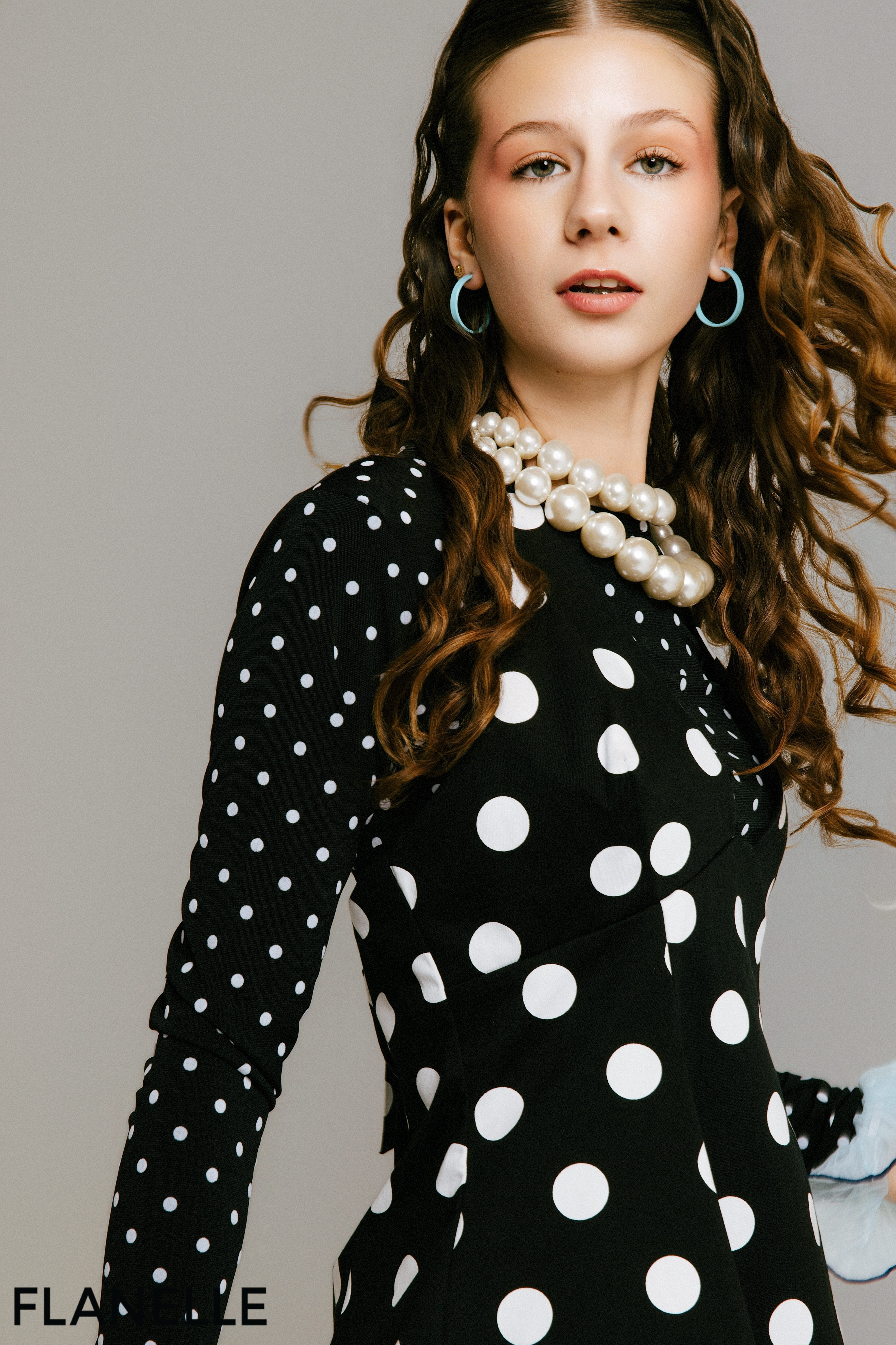 Woman in black polka dot dress with pearl necklace and turquoise hoop earrings.