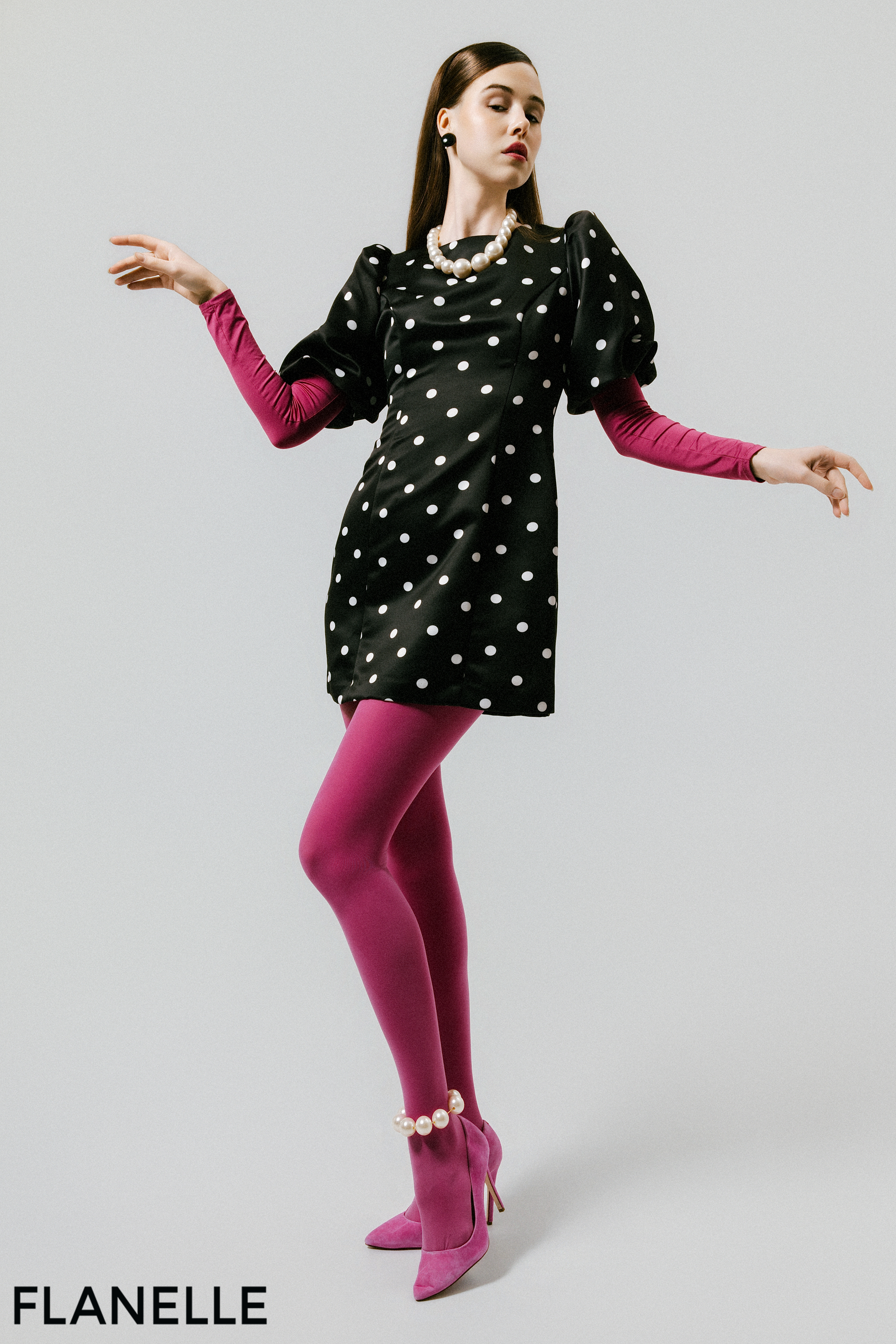 Model in polka dot dress, pink tights, and heels posing elegantly.