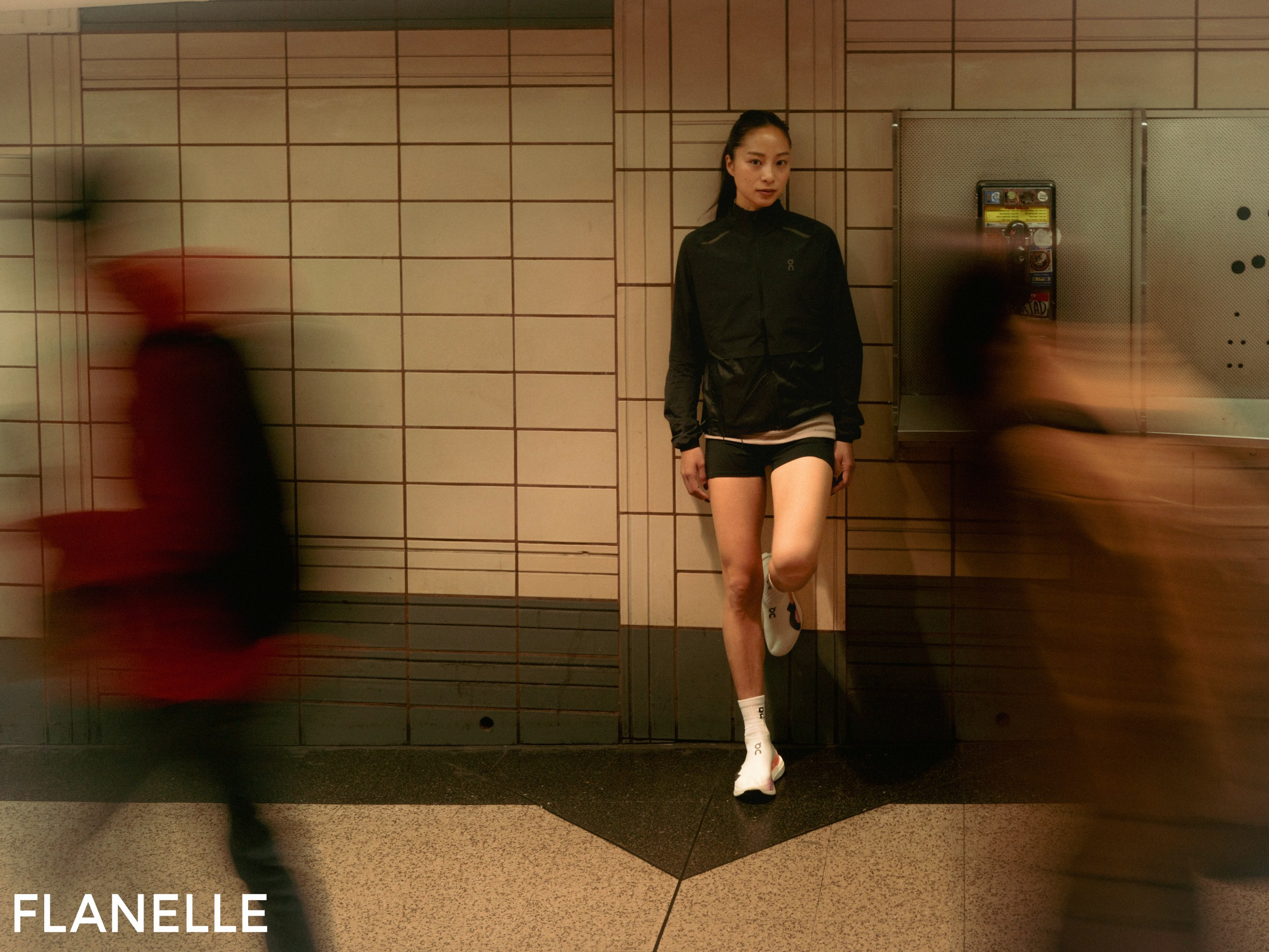 Runner in urban setting, blurred motion, wearing black jacket and shorts.