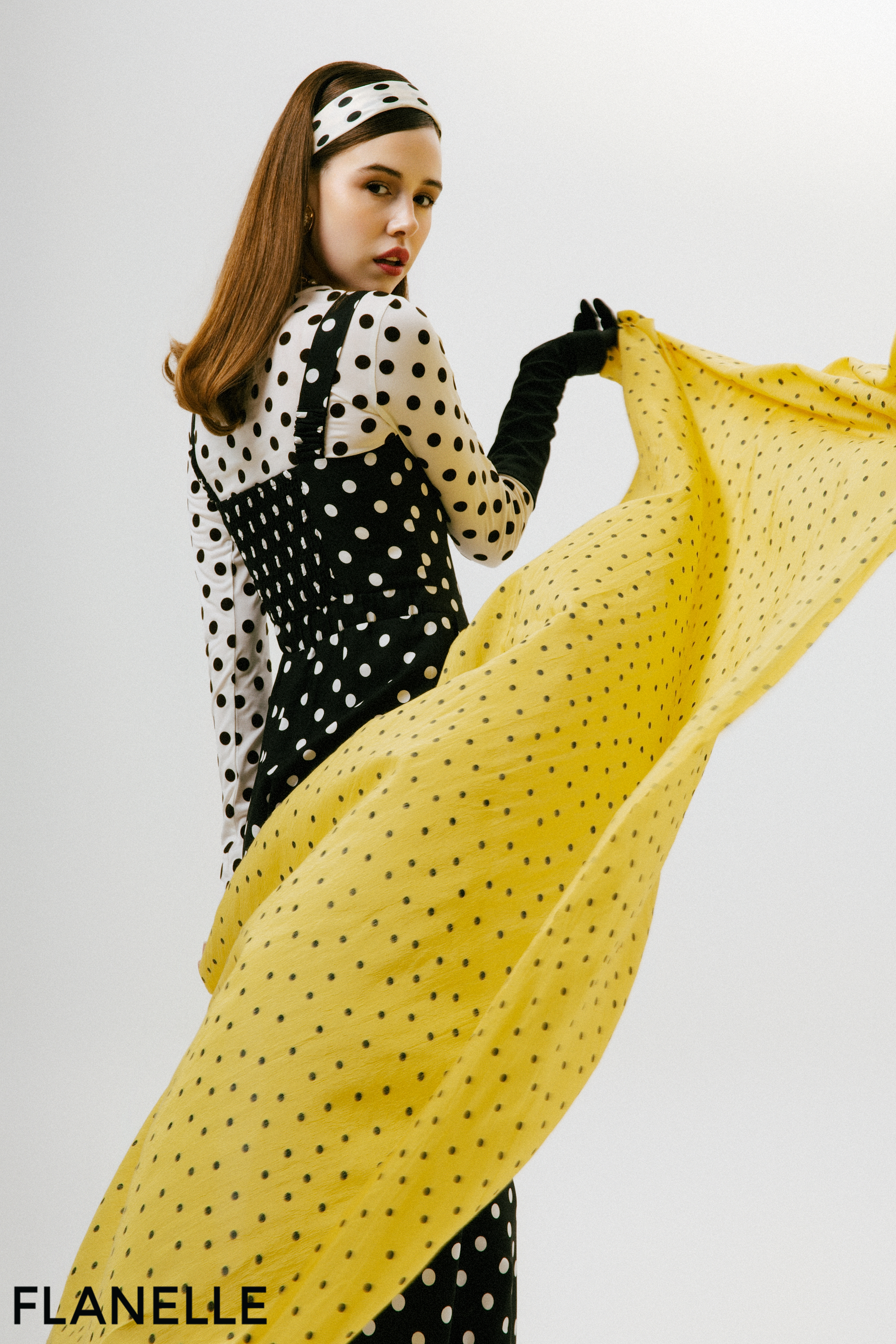 Fashion model in polka dot outfit with flowing yellow scarf.