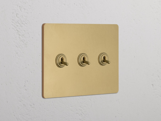 Gold triple toggle light switch on textured white wall.