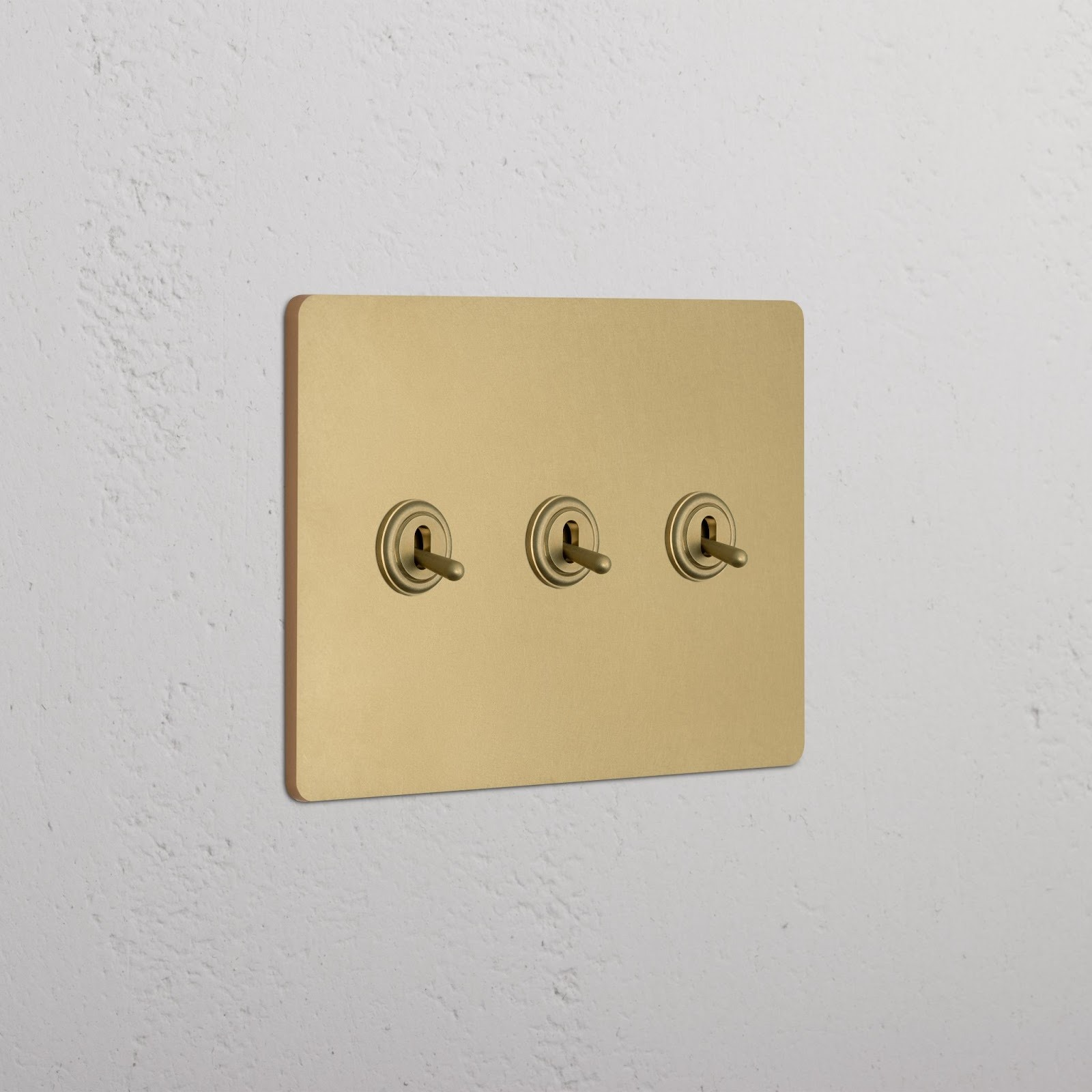 Gold triple toggle light switch on textured white wall.
