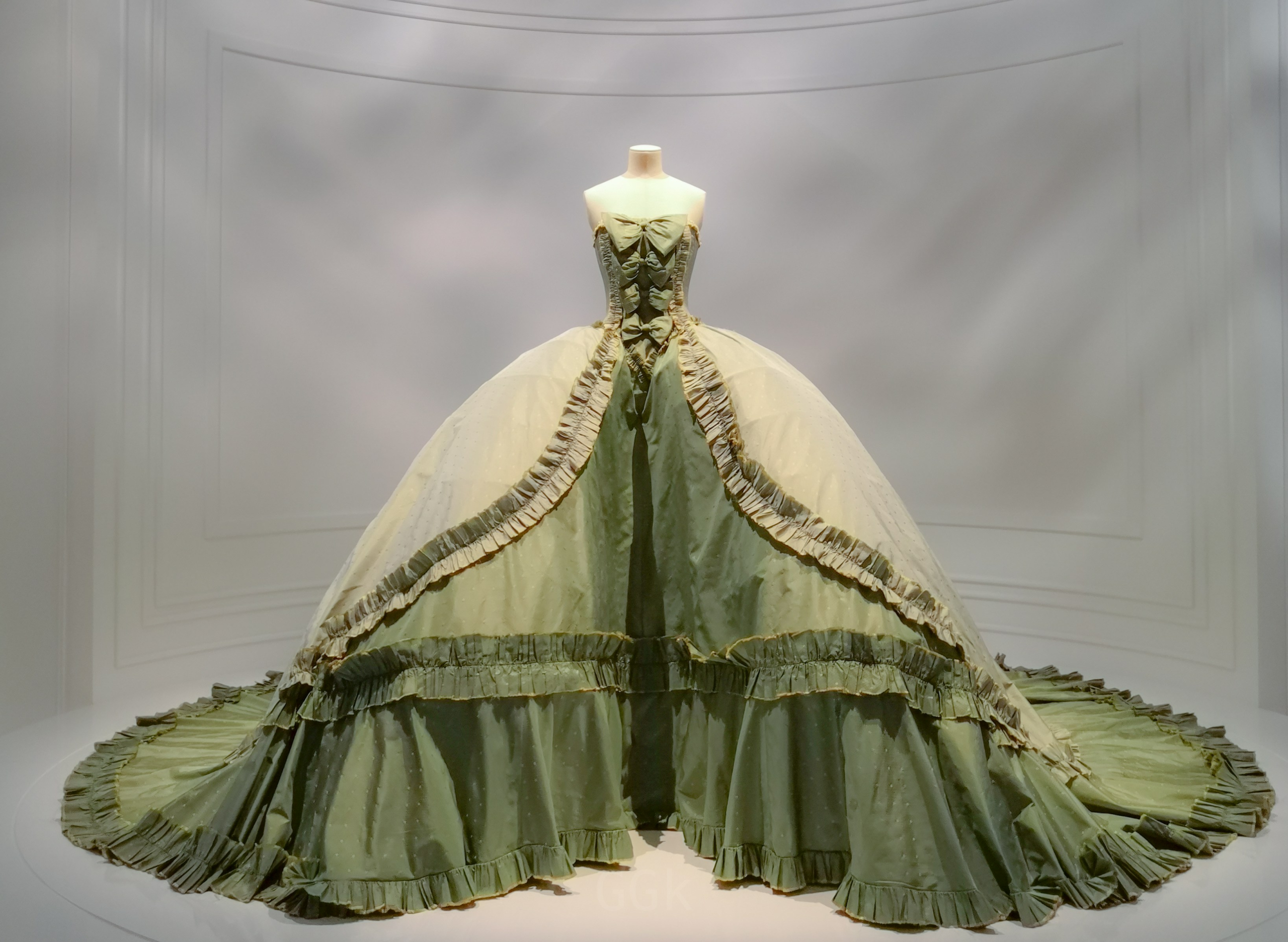 Elegant green and beige ball gown on display in a minimalist setting.