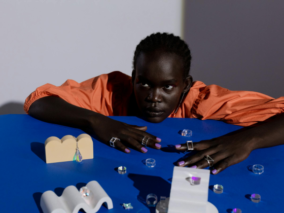 Model in orange with jewelry on blue table, creative studio fashion shot.